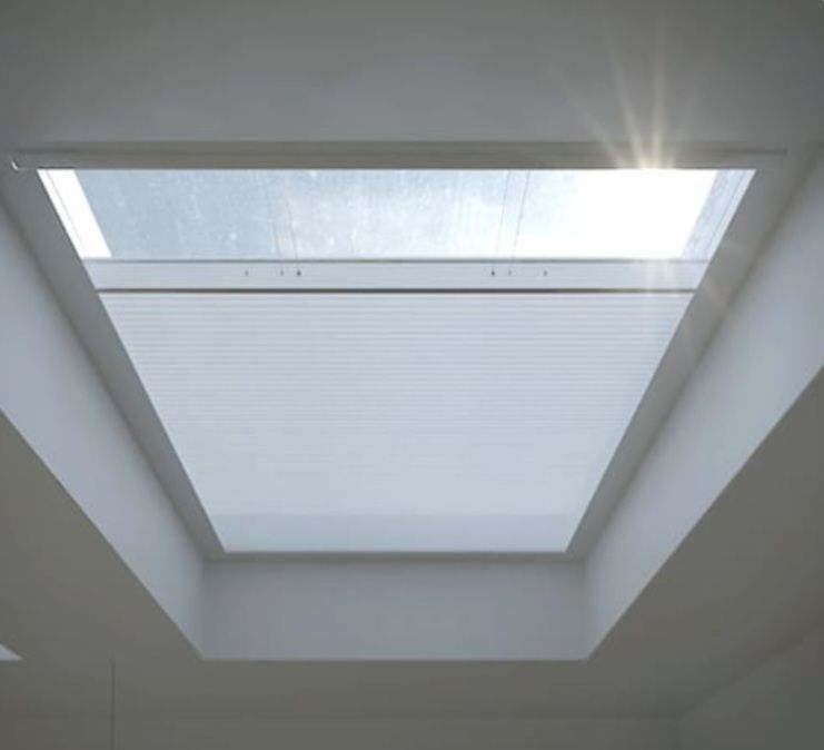 Skylight with a pleated shade, partially open, letting in bright sunlight. Angled ceiling.