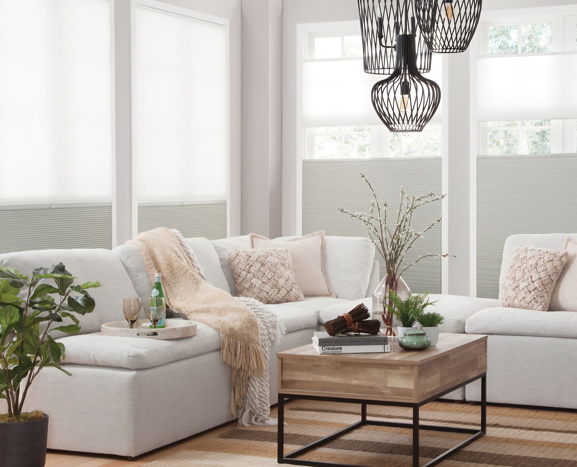 Living room with white sectional sofa, neutral decor, and large windows with blinds.