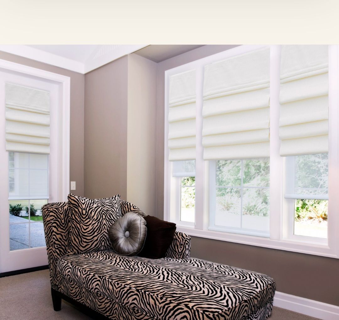 Chaise lounge with zebra print fabric in a room with neutral walls and cream-colored roman shades.