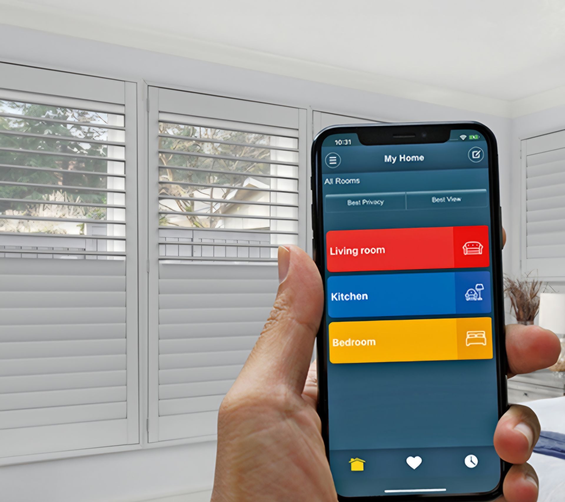 Hand holding a smartphone displaying a smart home app to control shutters in a bright room.
