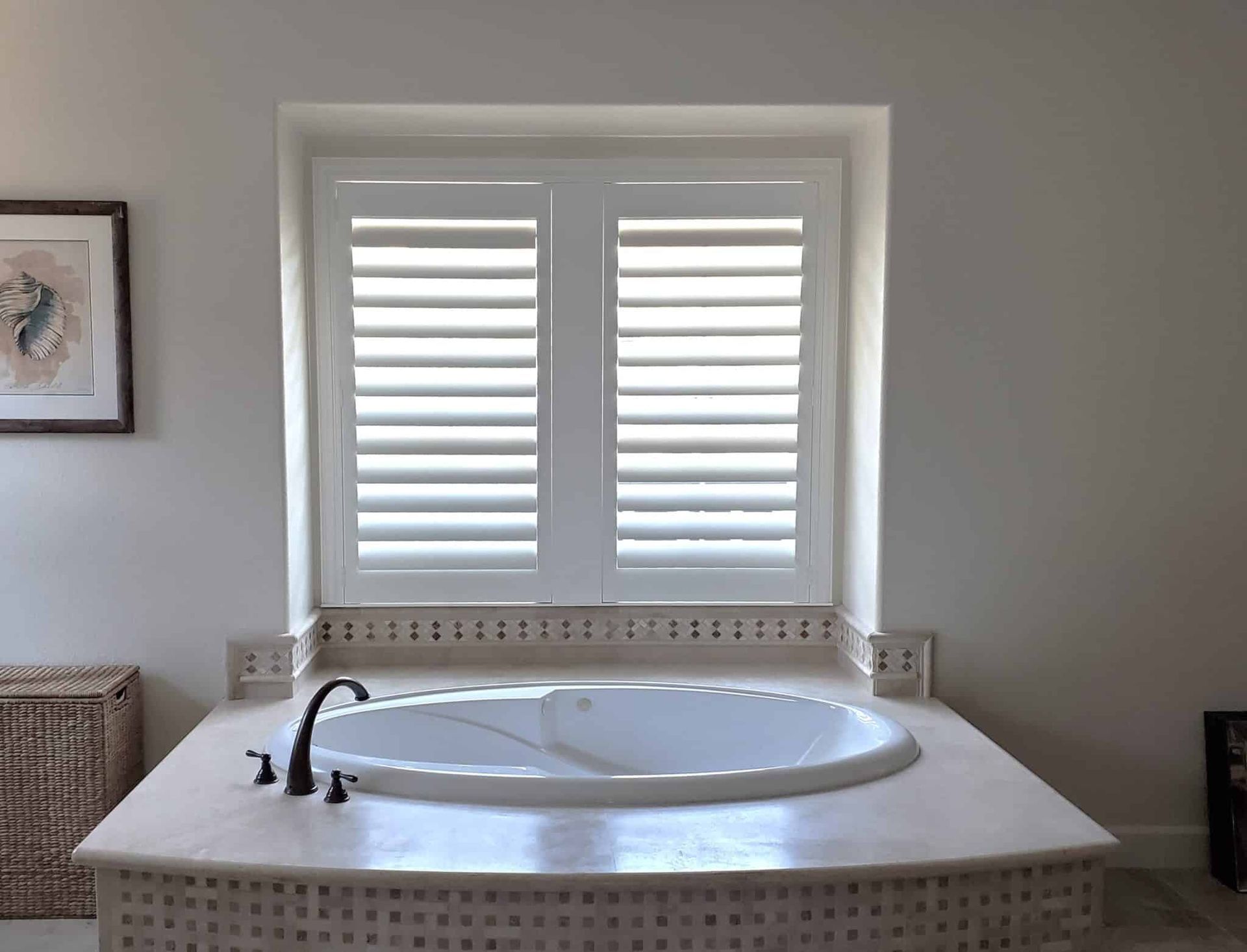 Bathroom with oval tub, shutters, and artwork. Natural light fills the space, showcasing a serene setting.