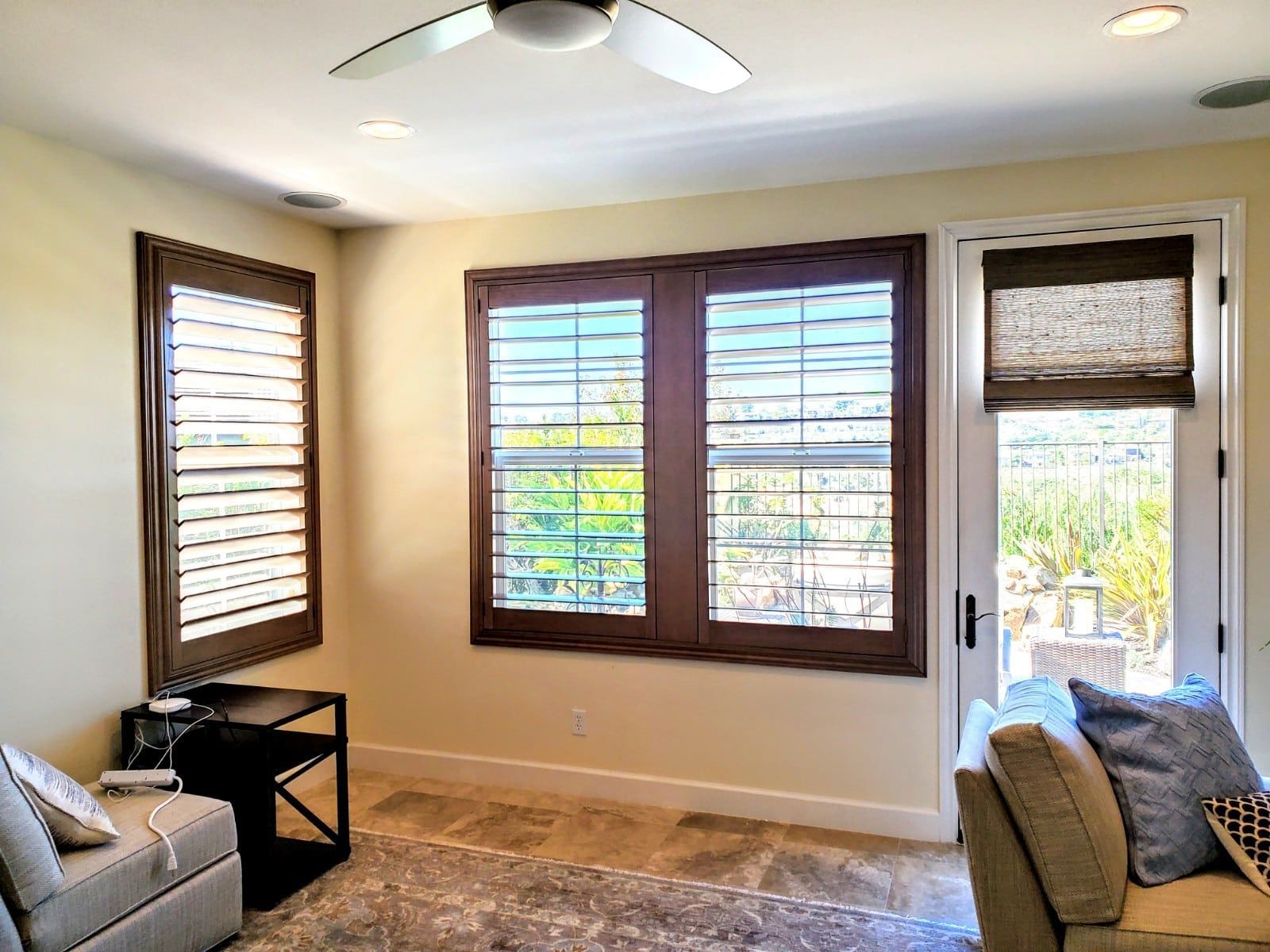 Room with windows and shutters, tan walls, and a ceiling fan.