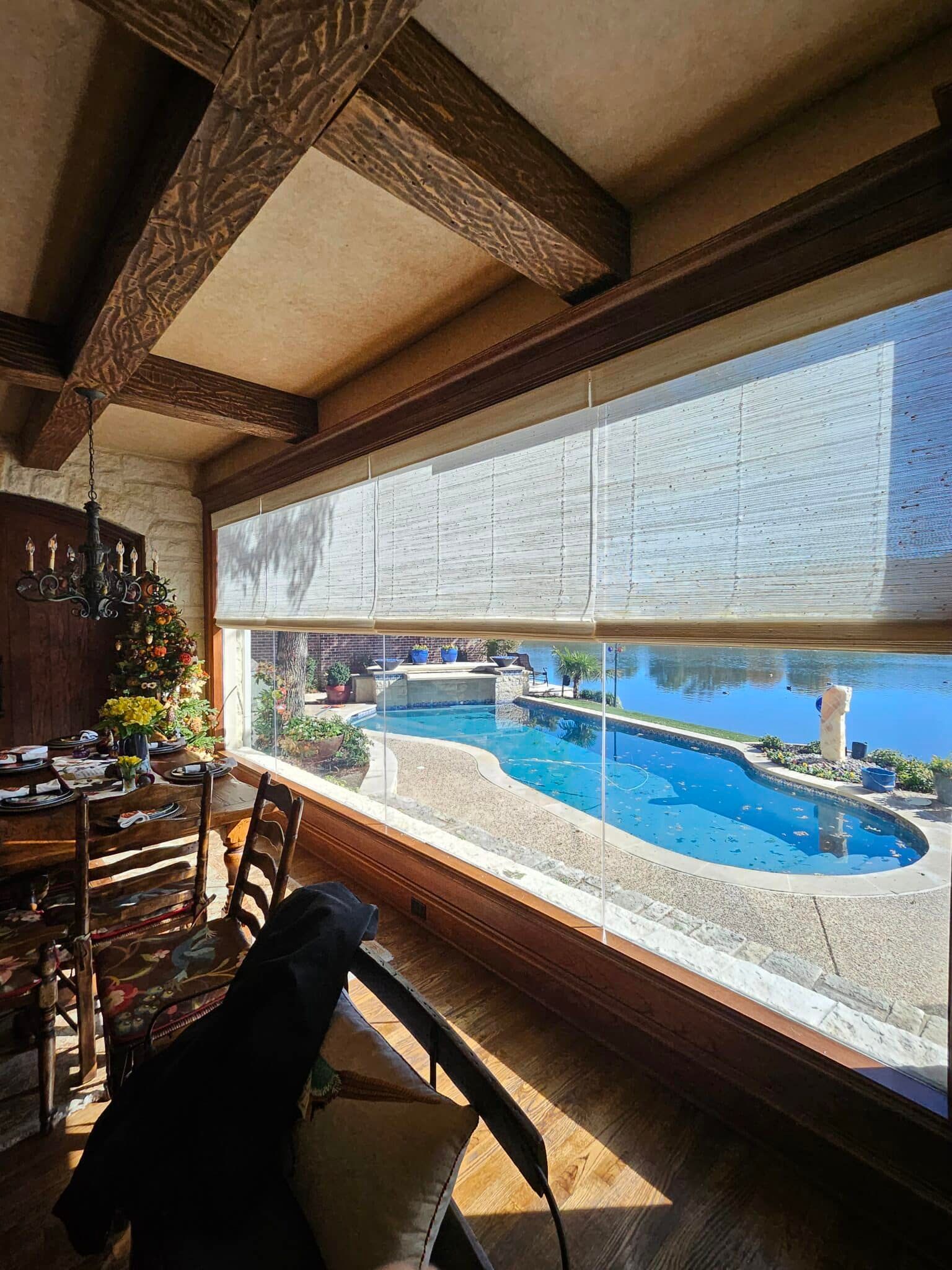 Dining room with pool view: wooden beams, table set for meal, pool and lake visible through window.