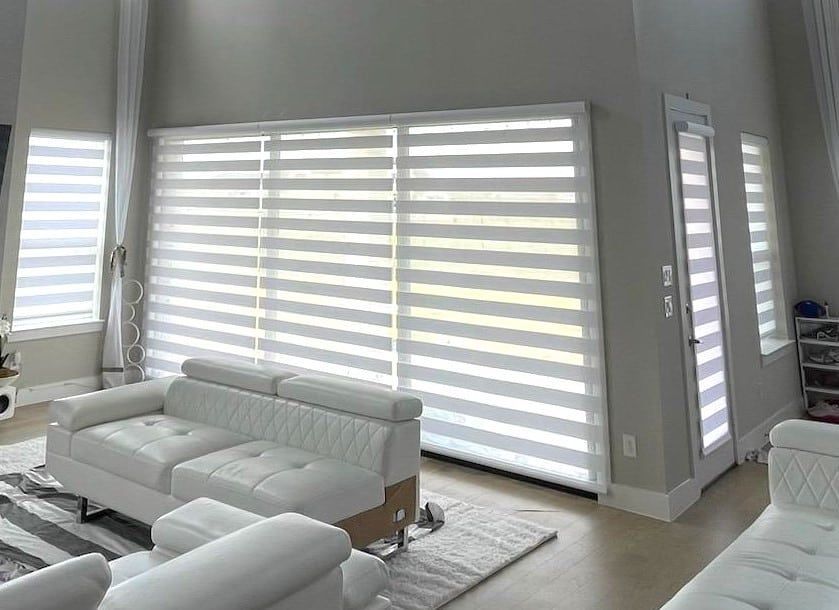 Living room with white sofas, horizontal striped blinds, and a door.