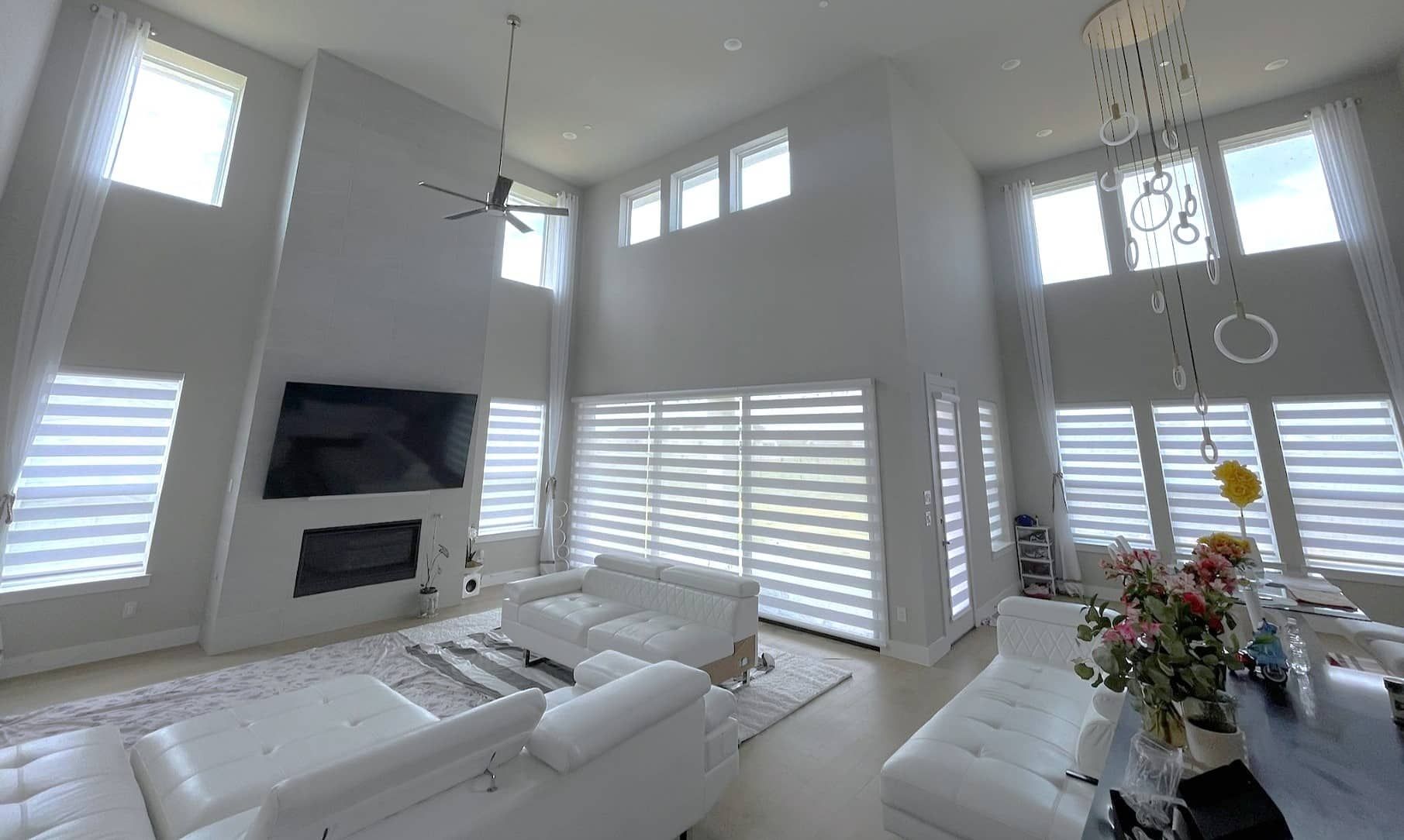 Spacious, modern living room with high ceilings, white walls, and large windows with blinds.