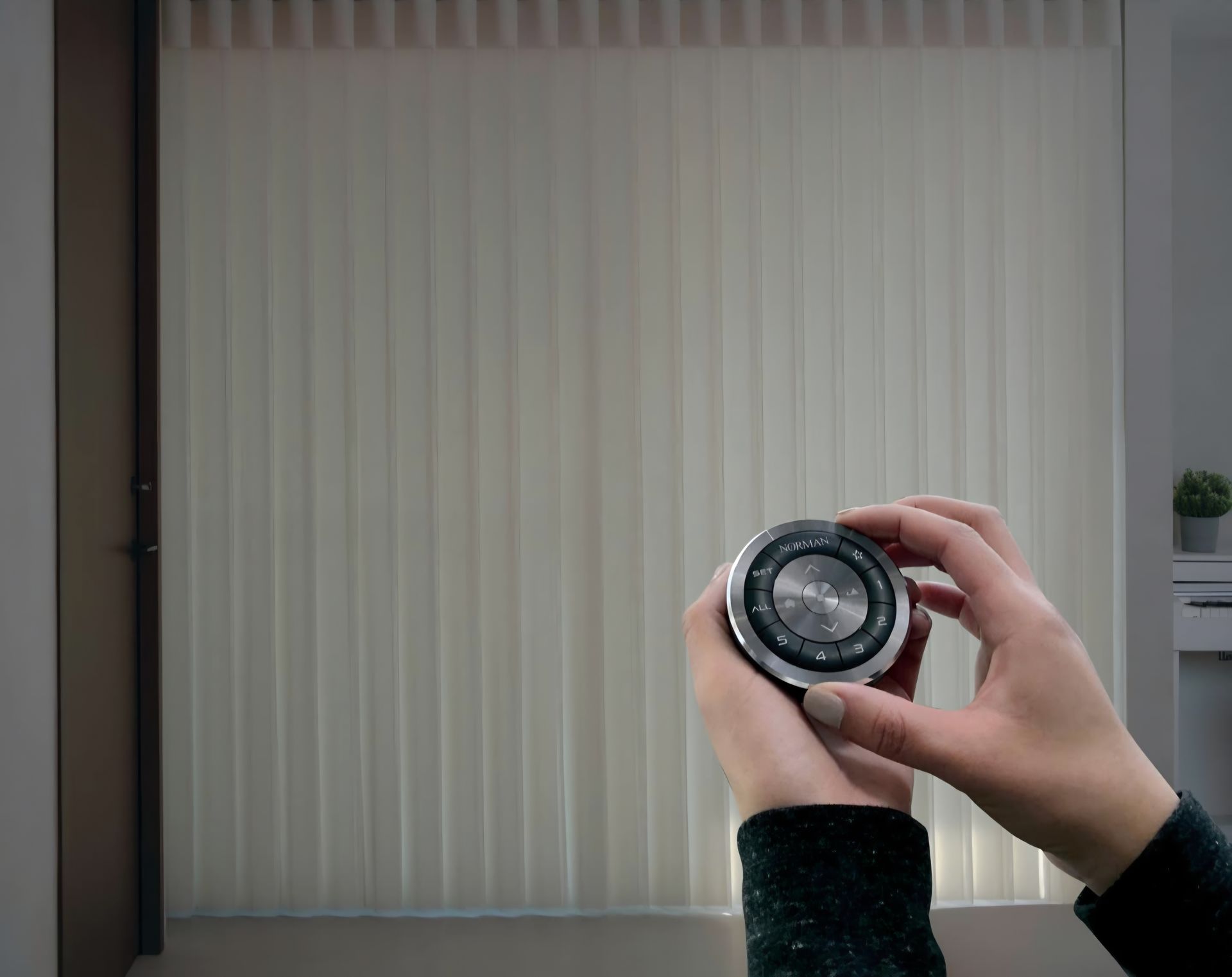 Person adjusting vertical blinds with a remote. Blinds are beige. Indoor setting.