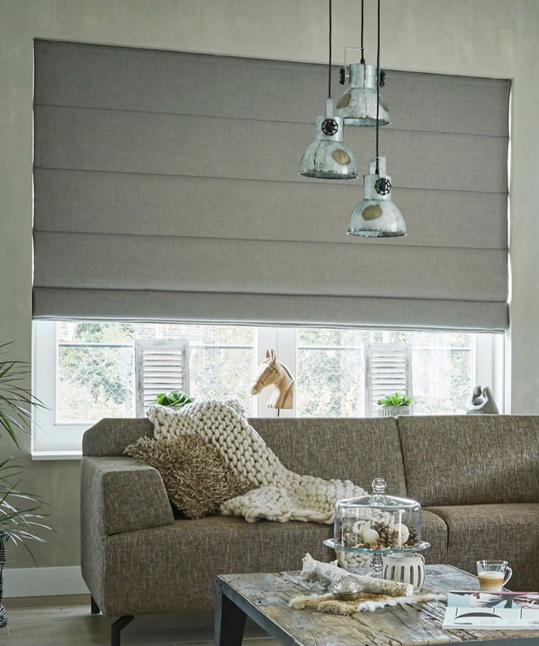 Gray Roman shade over a window with a couch and hanging lights, creating a cozy living room.