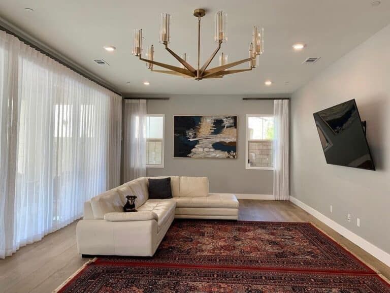 Living room with cream sectional, patterned rug, TV, artwork, and gold chandelier.