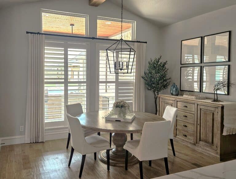Dining room with white shutters, a round table with chairs, and a light-colored wooden cabinet.