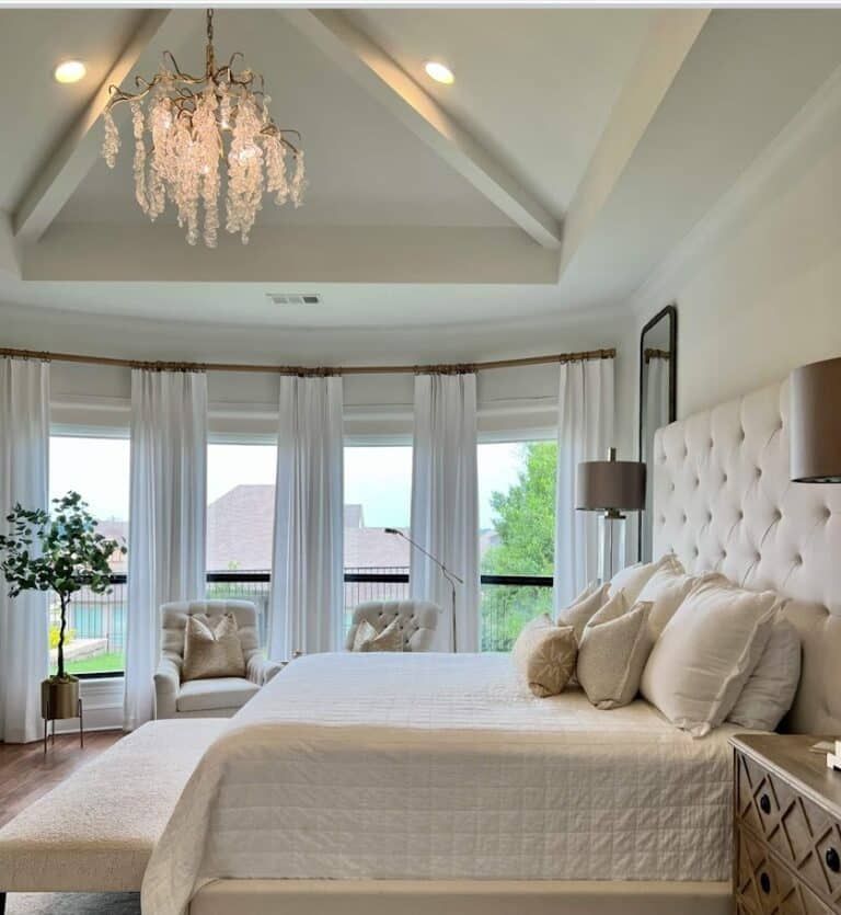 Elegant white bedroom with large bed, chandelier, and bay windows with white curtains.