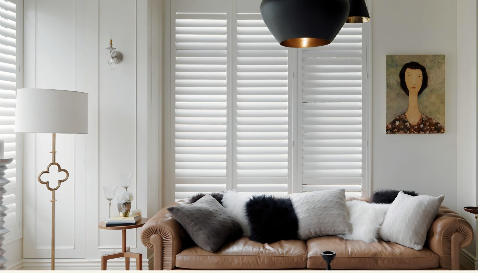 Living room with leather sofa, white shutters, lamp, and artwork.