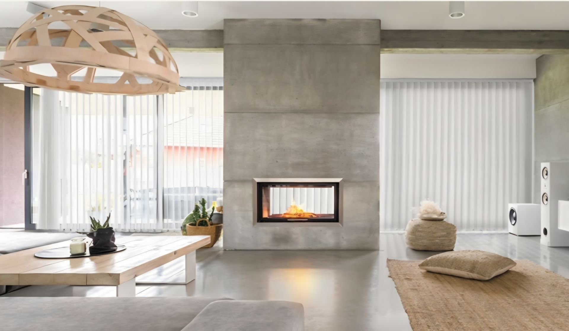 Modern living room with a concrete fireplace, vertical blinds, and a wooden light fixture.
