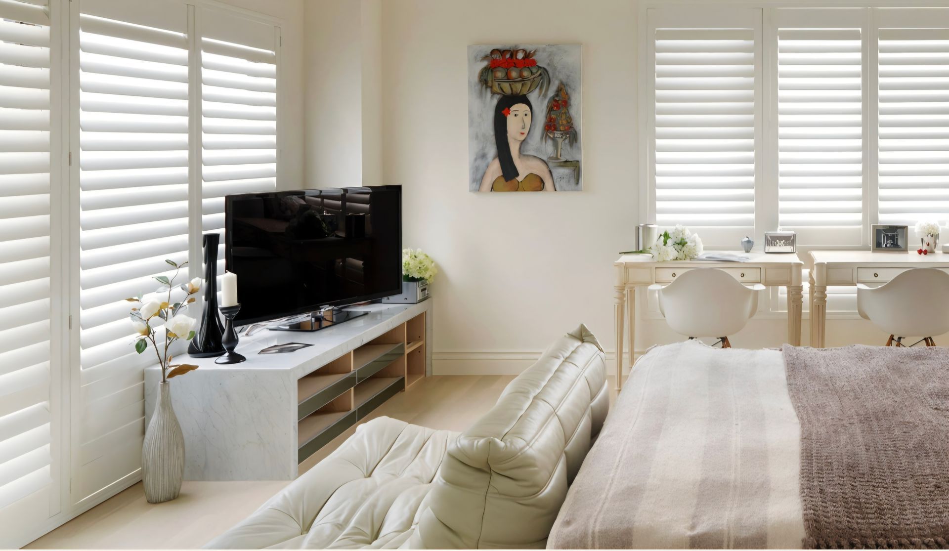 Bedroom with white shutters, marble TV stand, and painting.