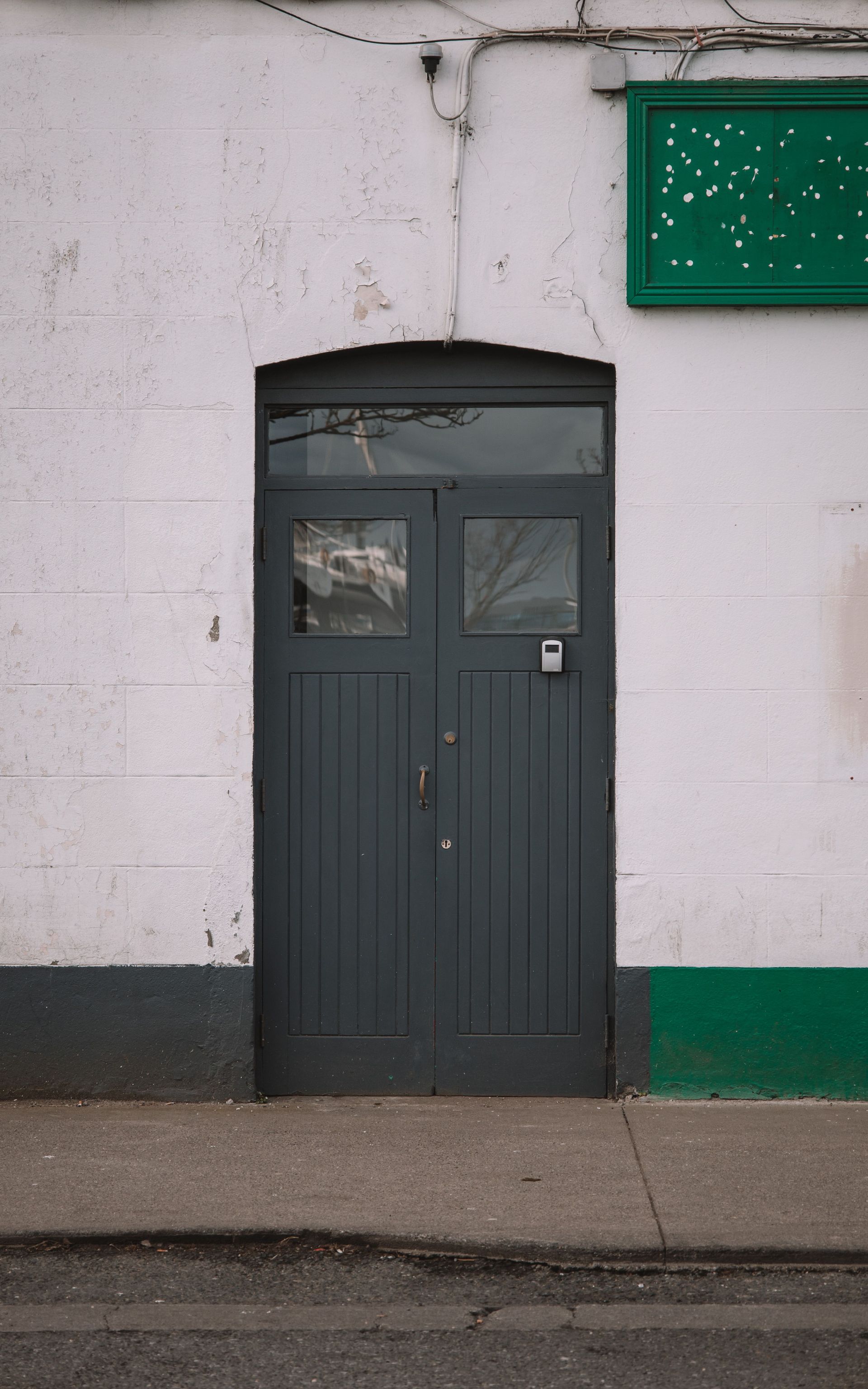 Glass double doors at a building entrance with posted notices and sunlight on the sidewalk