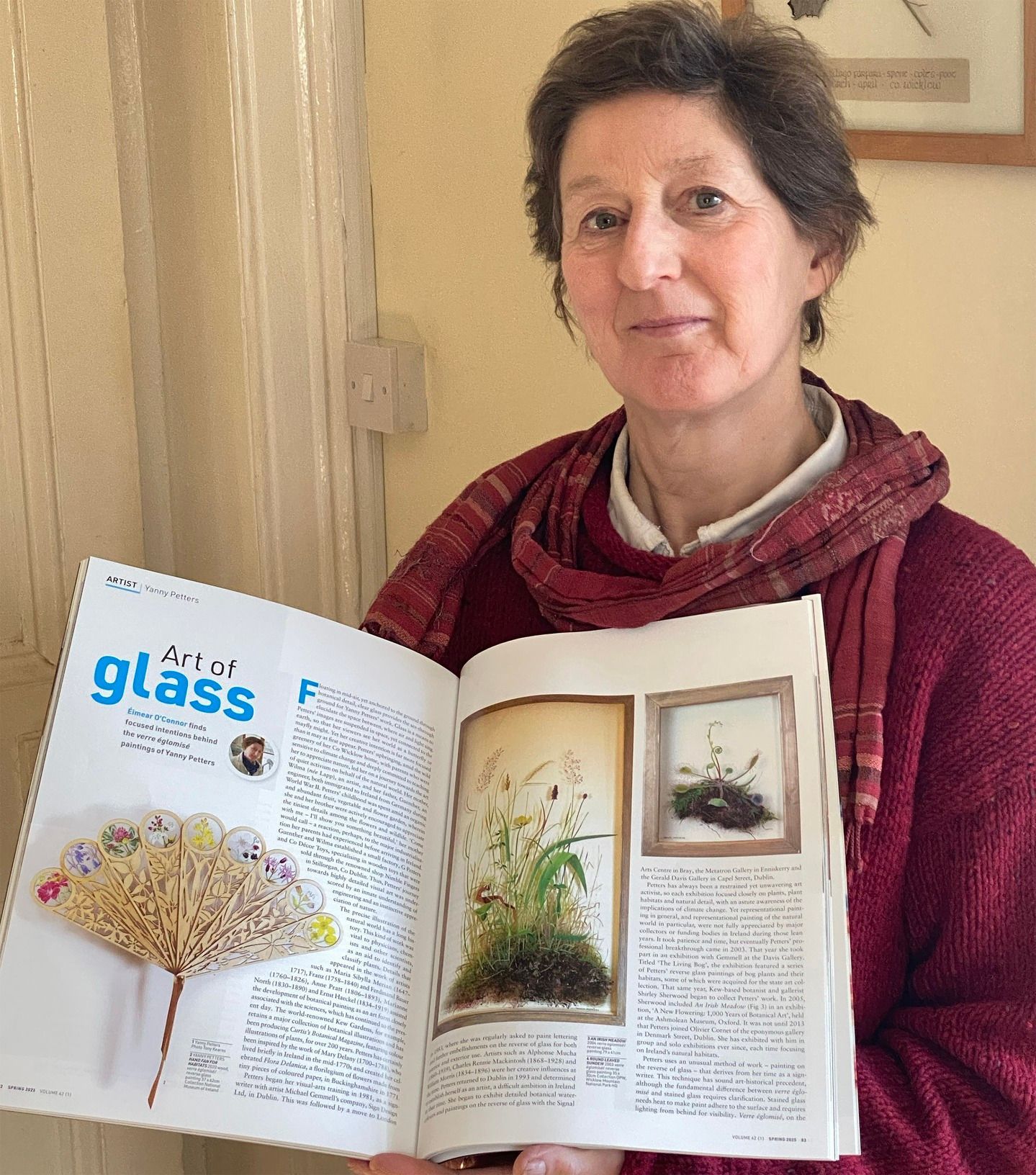 photo of Yanny Petters with a copy of the Irish Arts Review magazine, Spring 2025 edition, featuring Éimear O’Connor's review of the artist's glass art practice