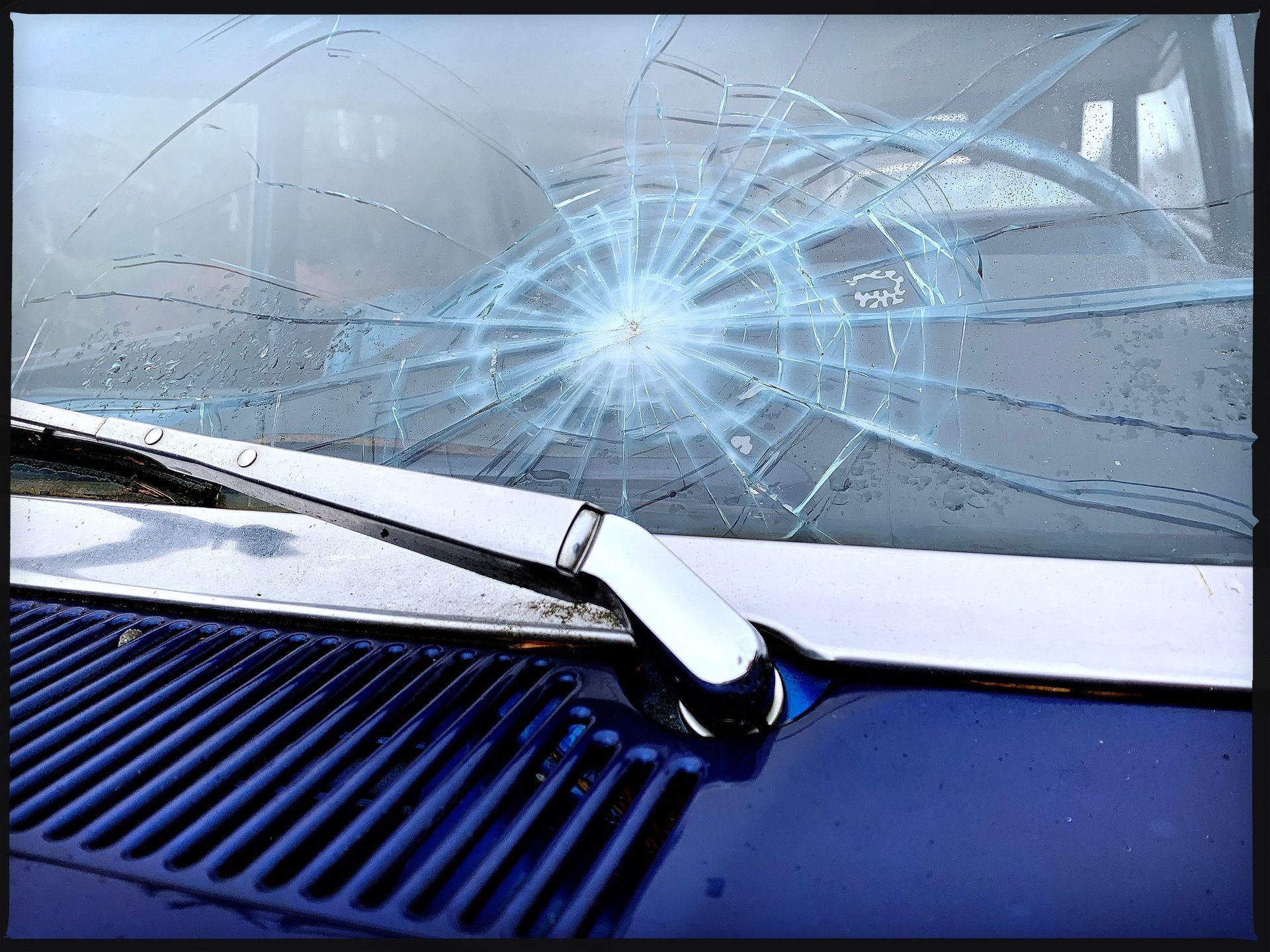 A car windscreen with a large circular crack and shattered glass near the wiper