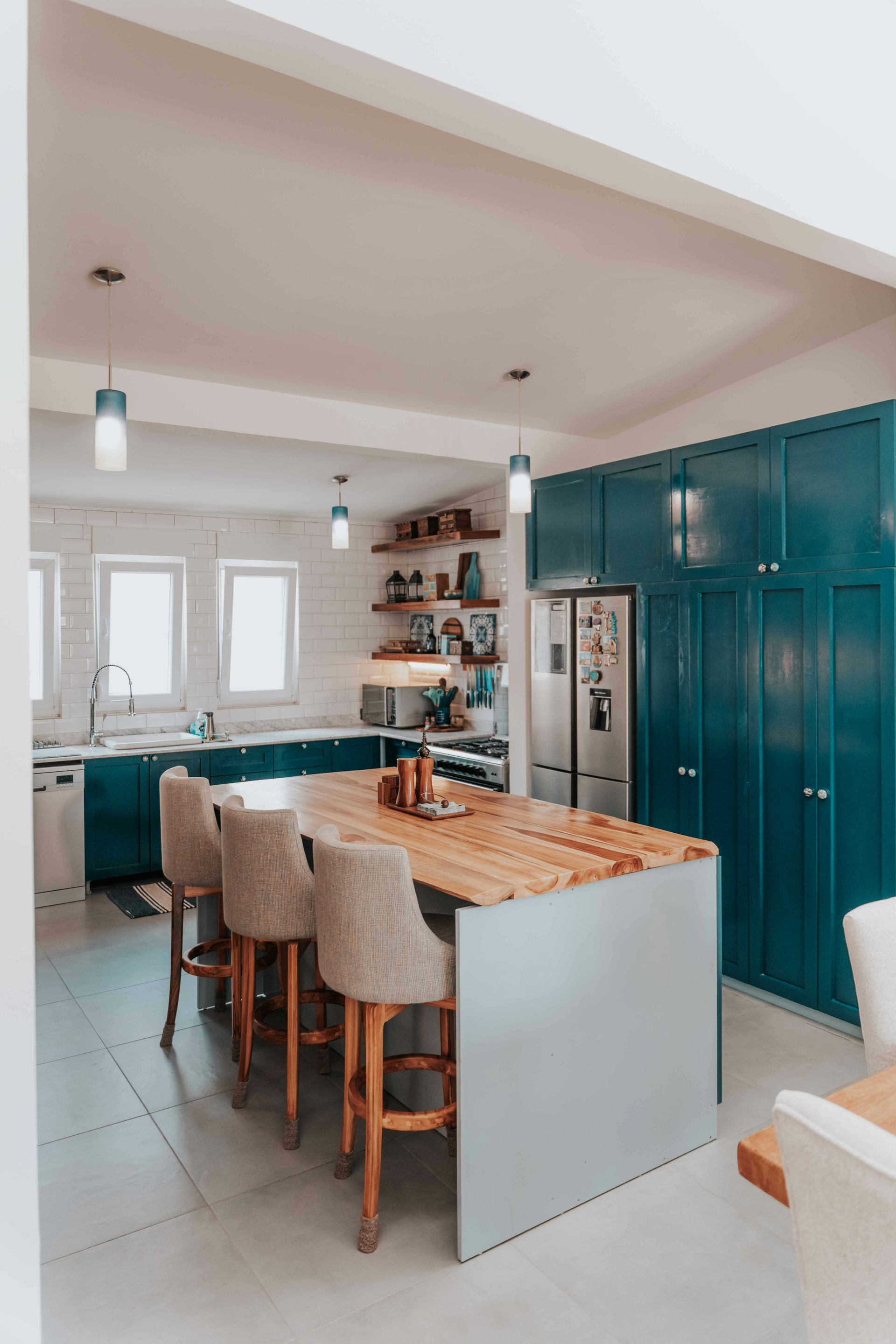 Modern kitchen with teal cabinets, wooden island with bar stools, and pendant lights.