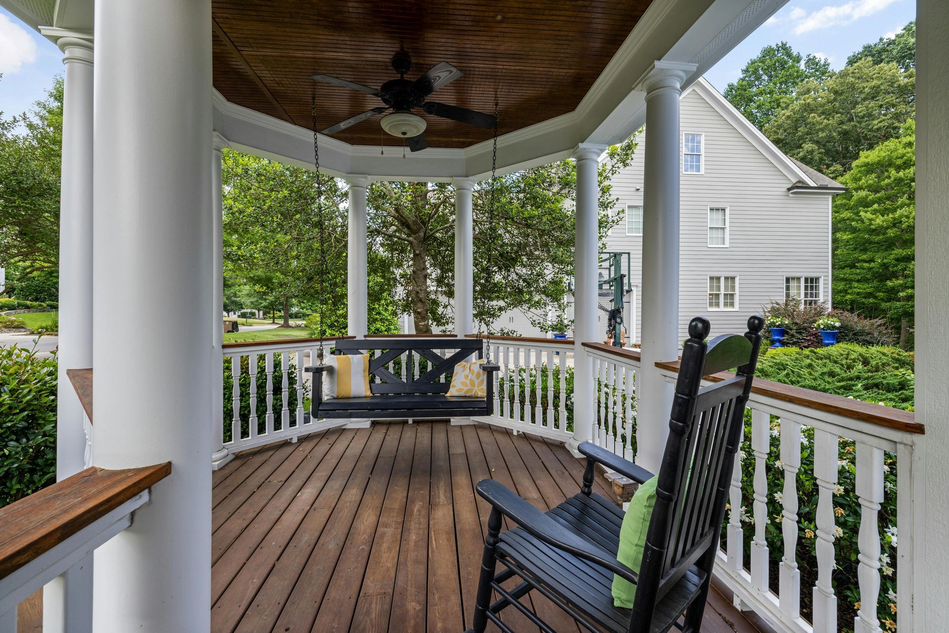 Wooden porch with swing and rocking chair, overlooking a yard and house.