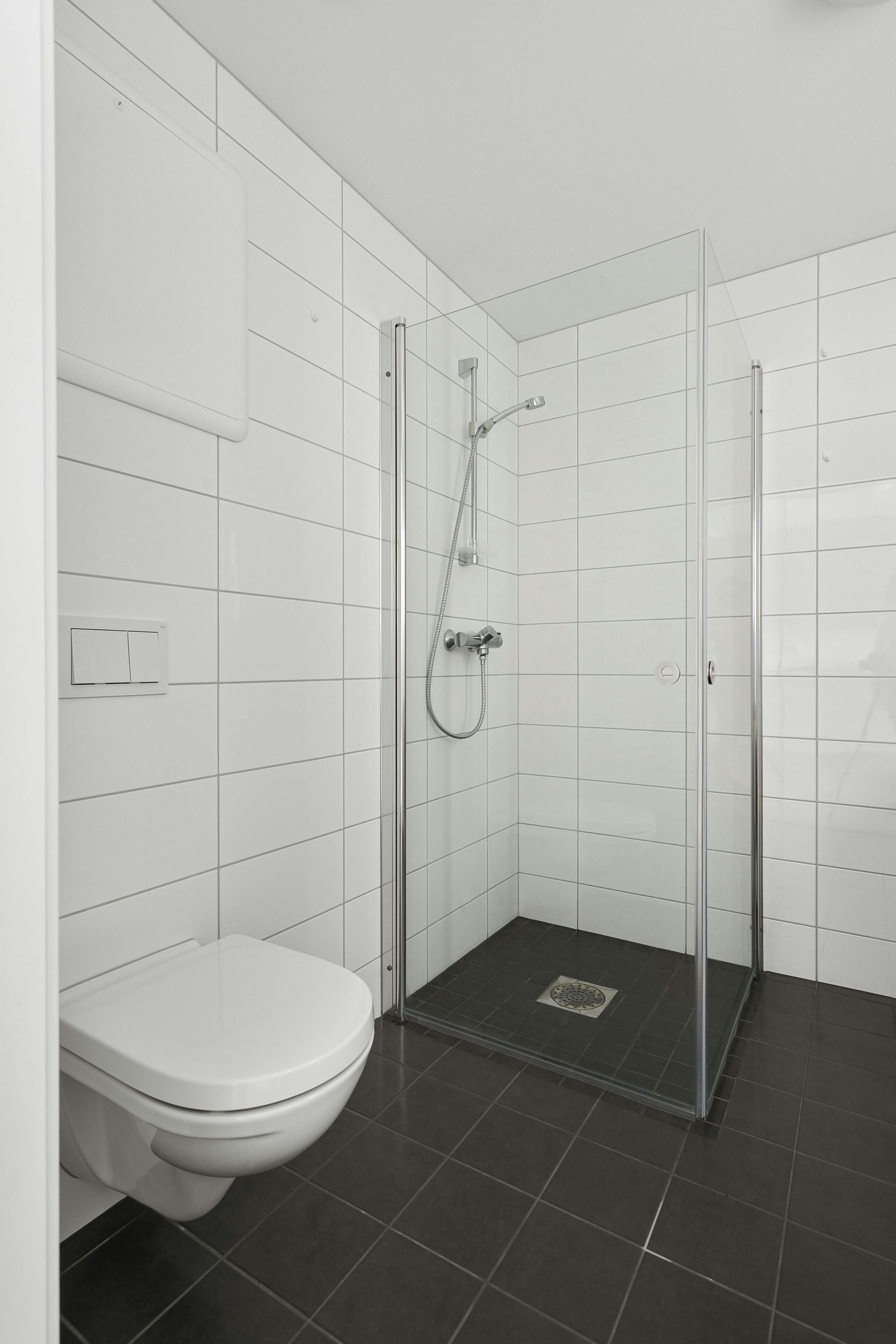 Bathroom with white tile walls, a toilet, and a glass shower enclosure with a dark floor.