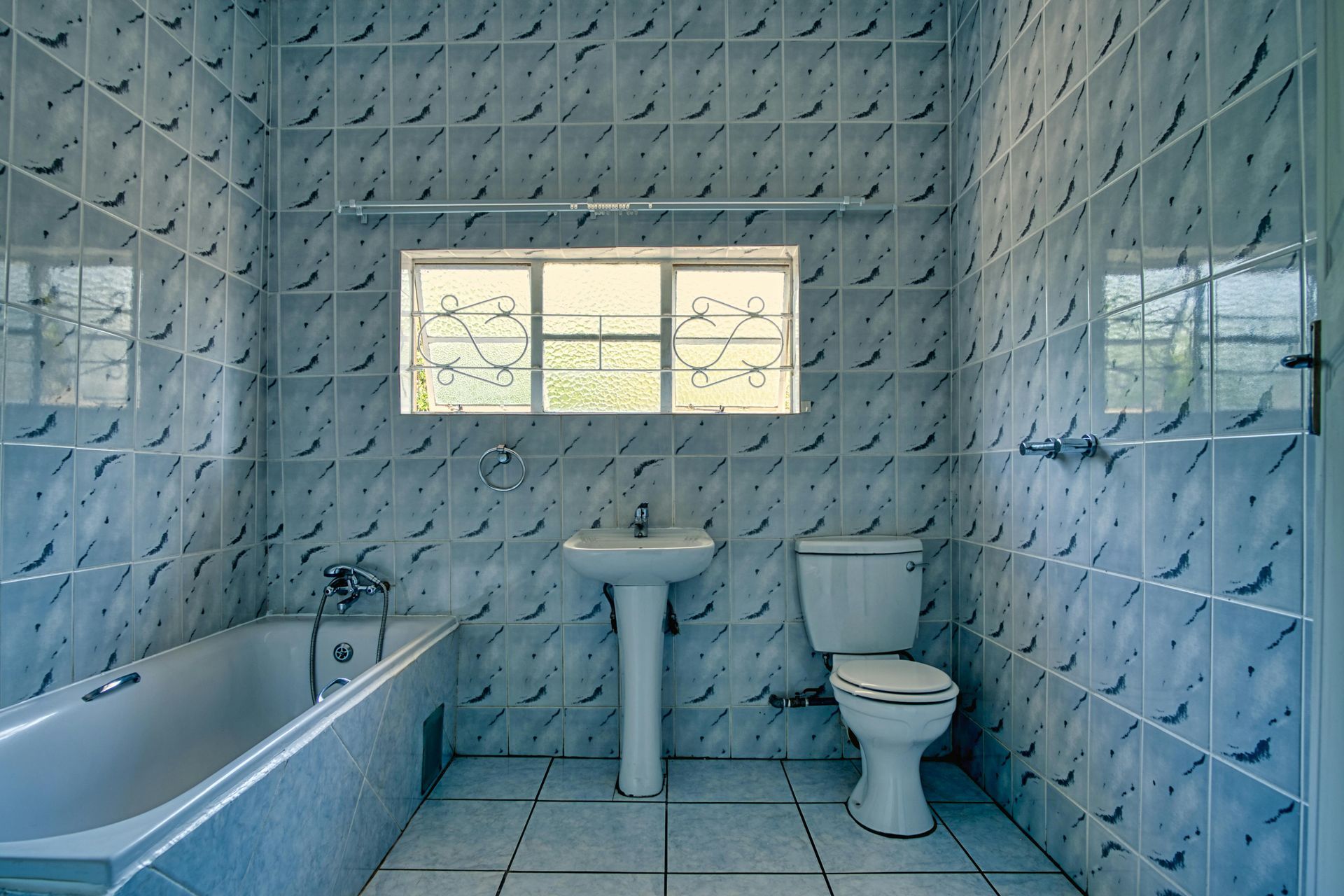 Bathroom with a bathtub, sink, and toilet, tiled walls, and a window with decorative bars.
