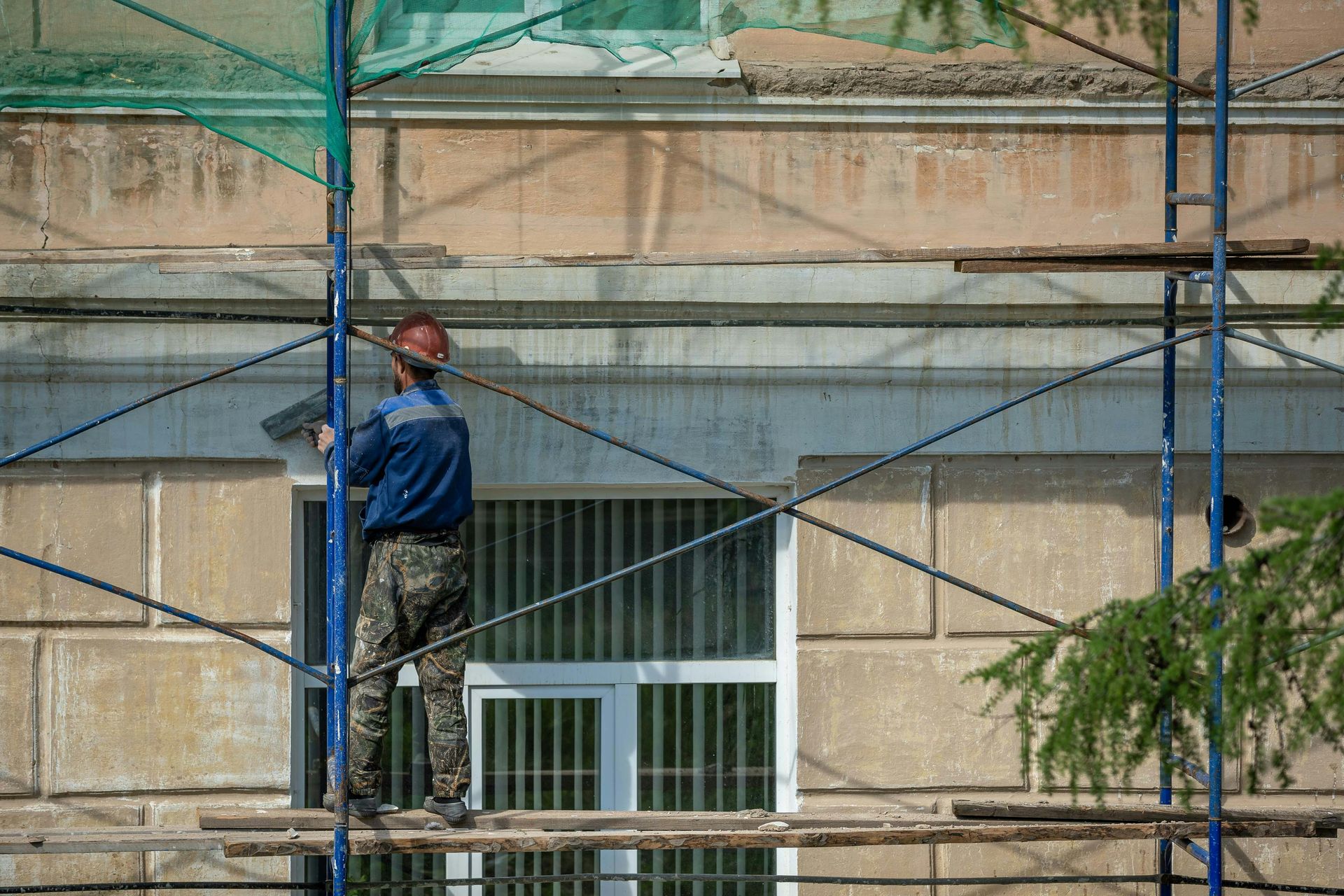 Construction worker on scaffolding repairs building facade.