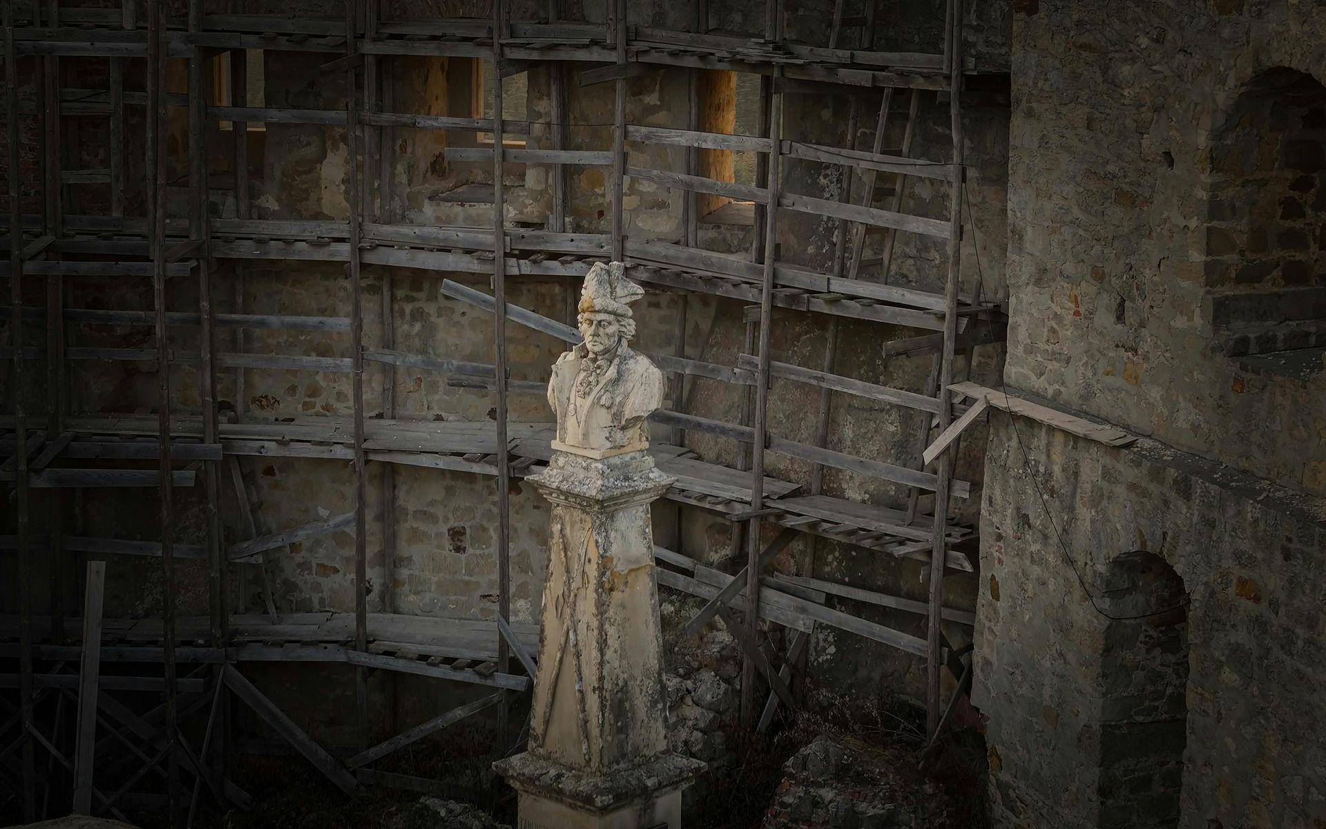 Stone statue on a pedestal, scaffolding in the background, possibly under restoration.