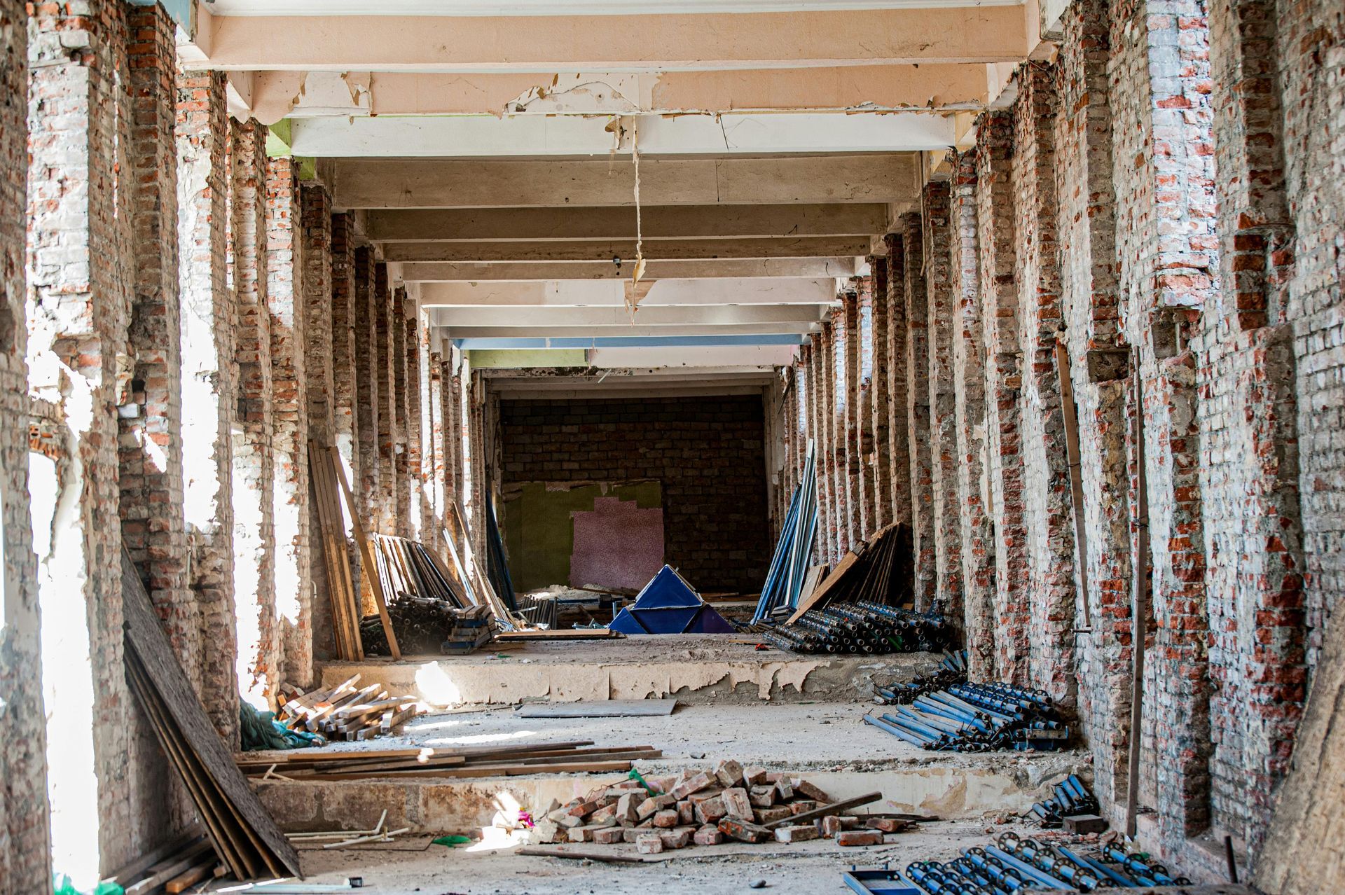 Corridor in a building undergoing demolition, showing exposed brick pillars and debris.