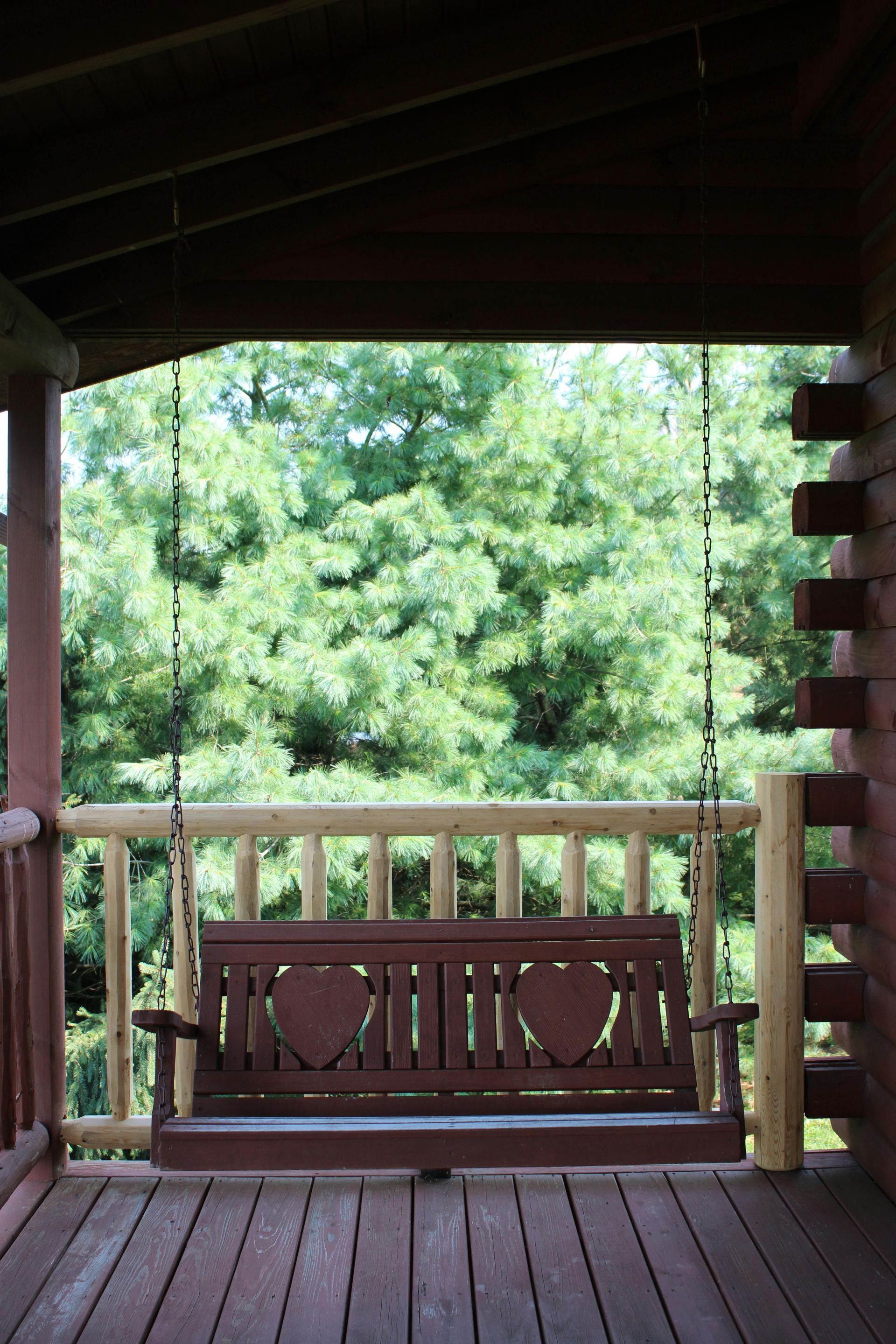 Wooden porch swing, framed by a log cabin's porch with a forest background.