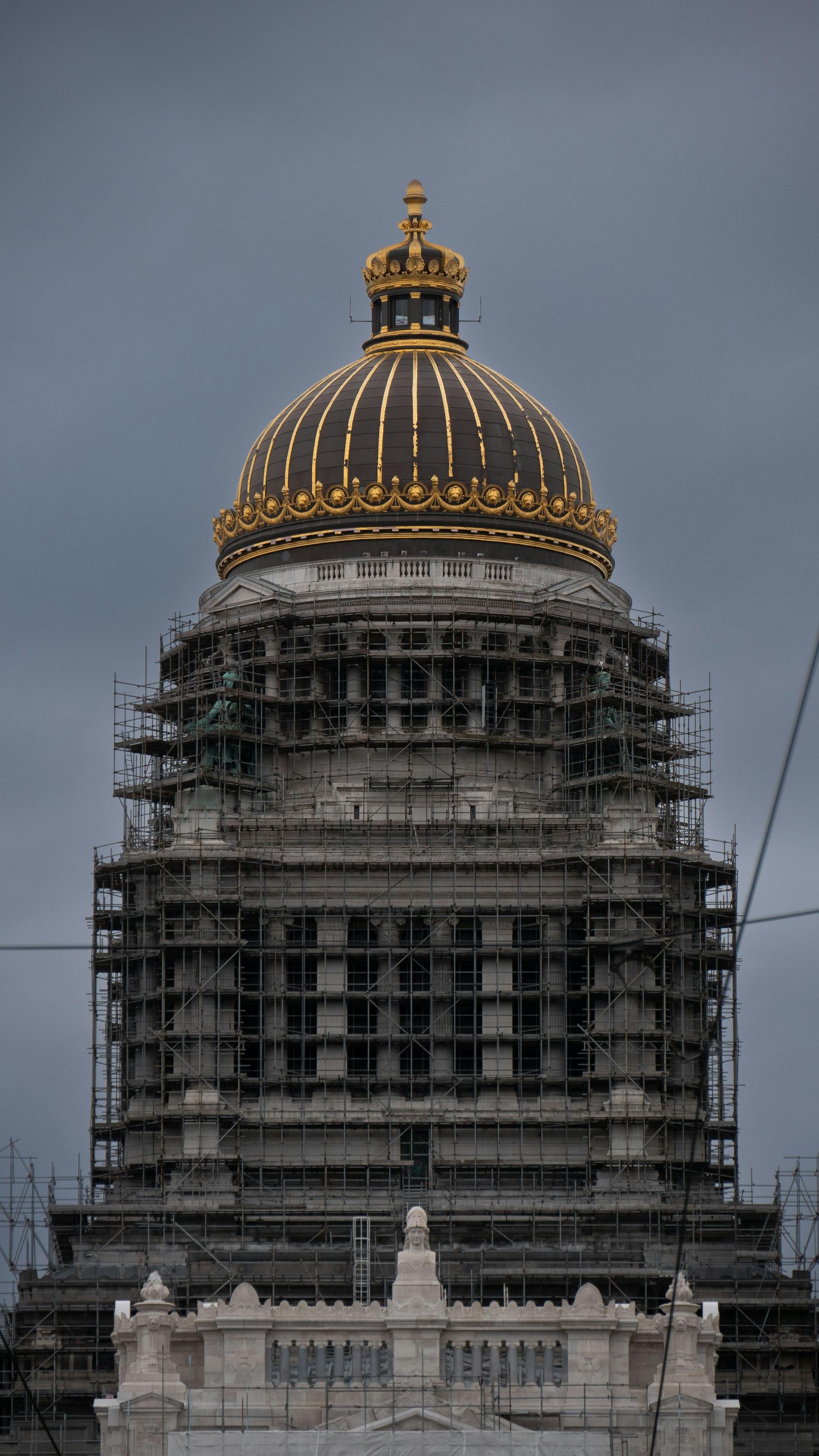 Brussels Palace of Justice dome under construction, scaffolding, gold top, against cloudy sky.