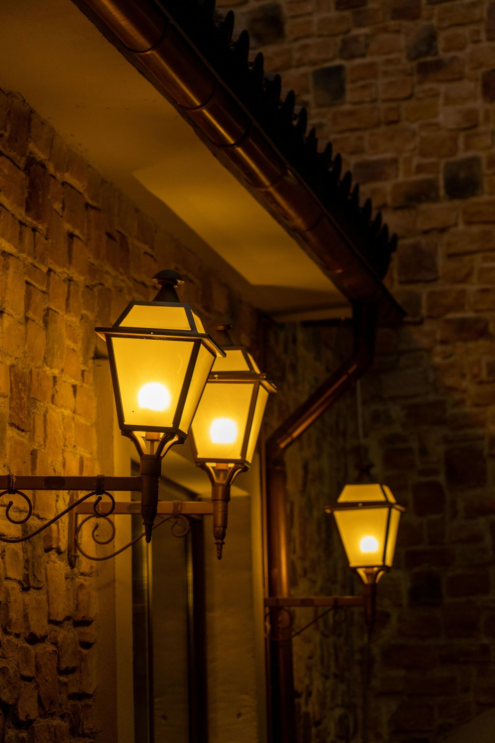 Three glowing street lamps mounted on a brick wall at night.