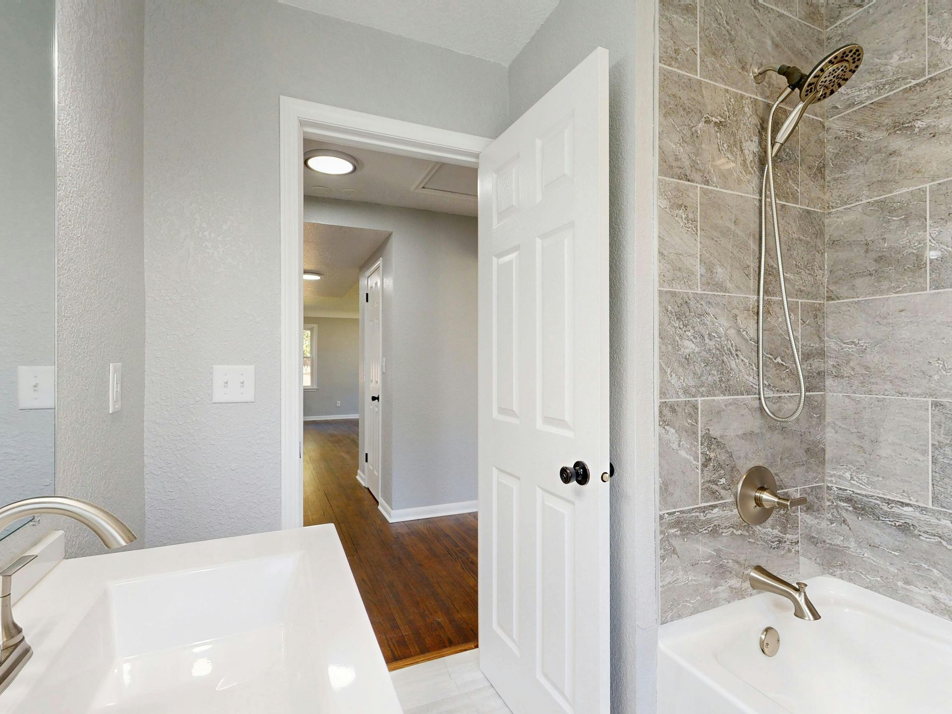 Bathroom interior with shower, vanity, and open door to hallway with wood floors.