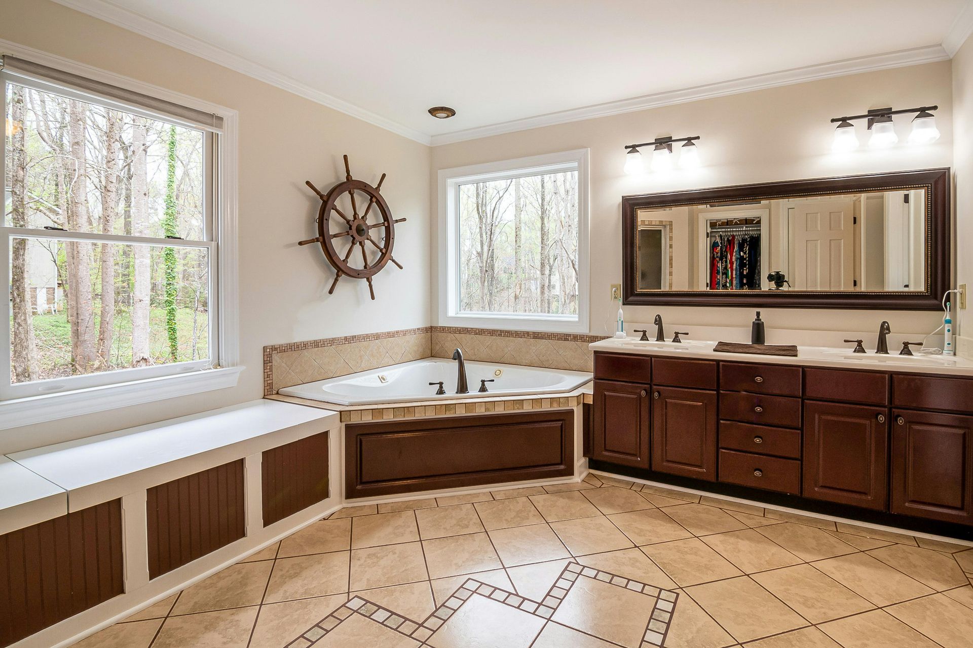Spacious bathroom with soaking tub, double vanity, large mirror, and nautical wheel decor.