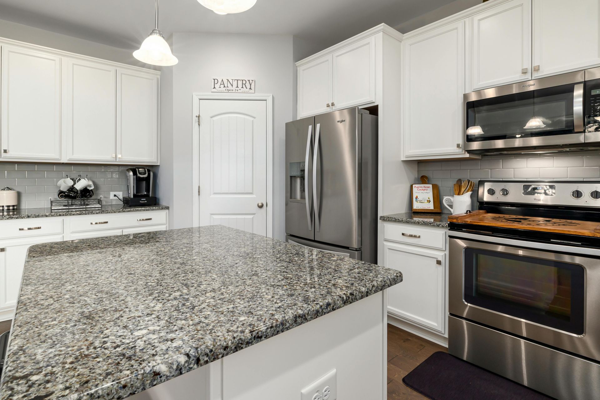 Kitchen with white cabinets, stainless steel appliances, and granite island countertop.