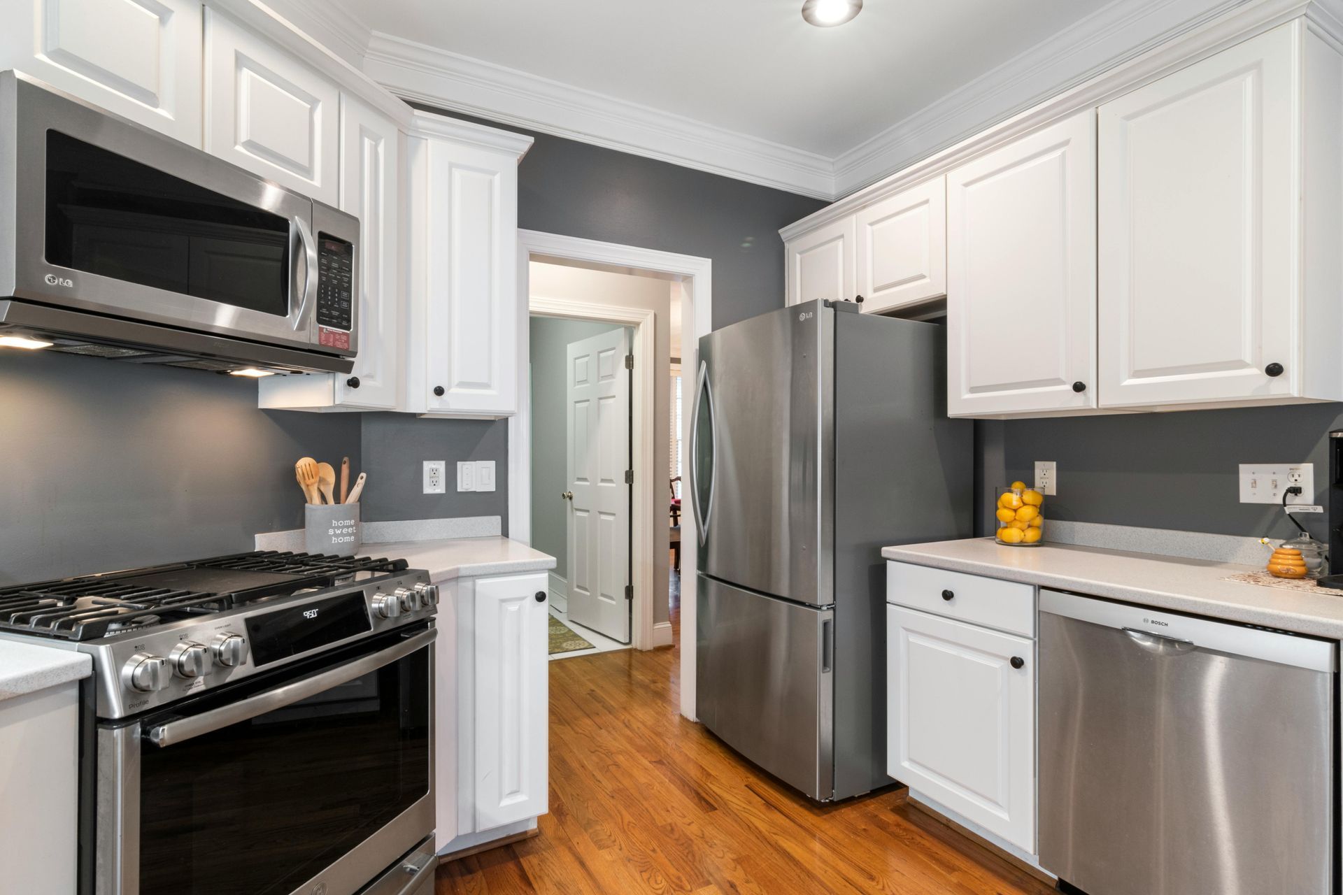 White kitchen with stainless steel appliances, grey walls, and hardwood floors.