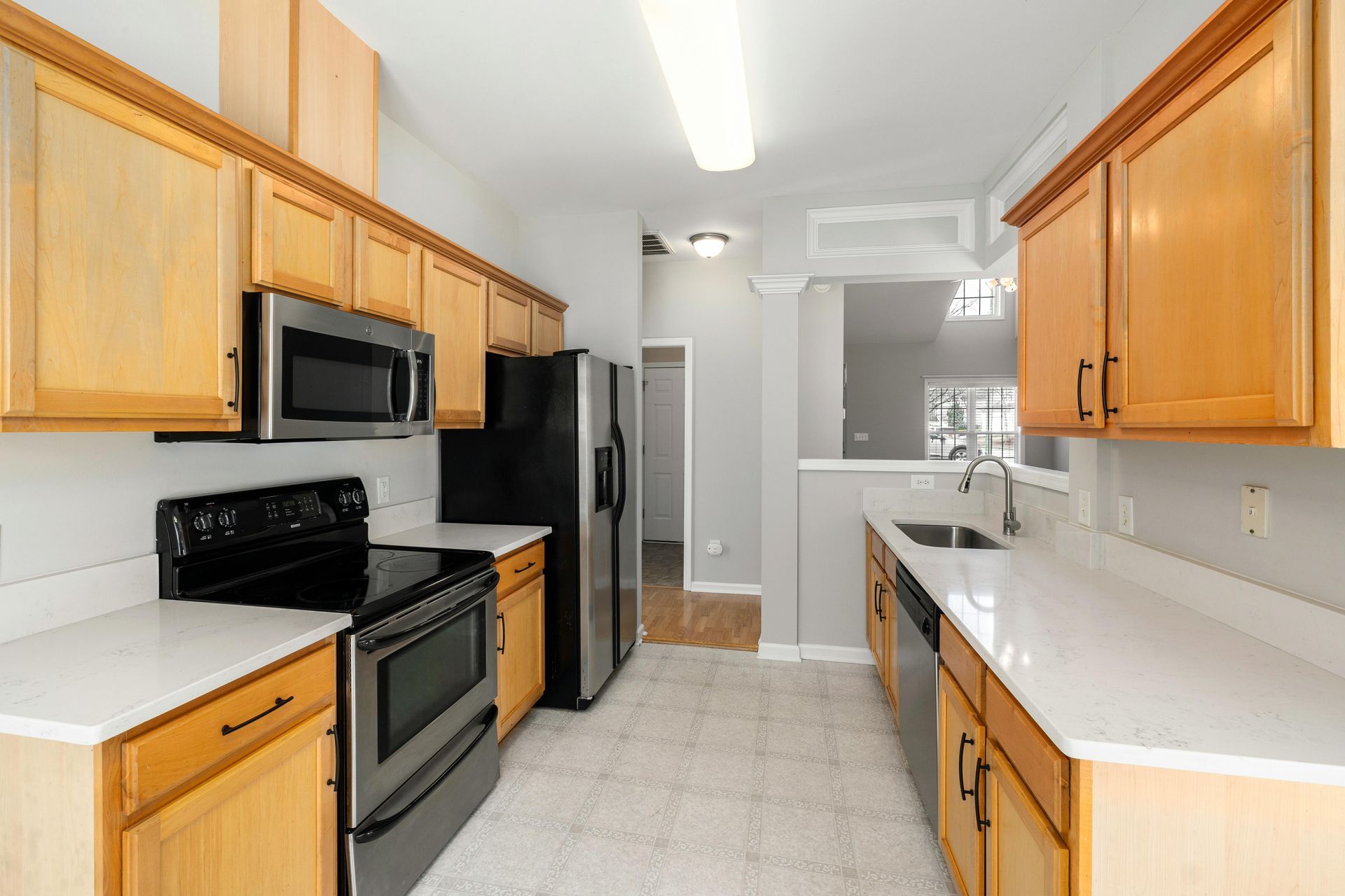Kitchen with light wood cabinets, stainless steel appliances, white countertops, and gray walls.