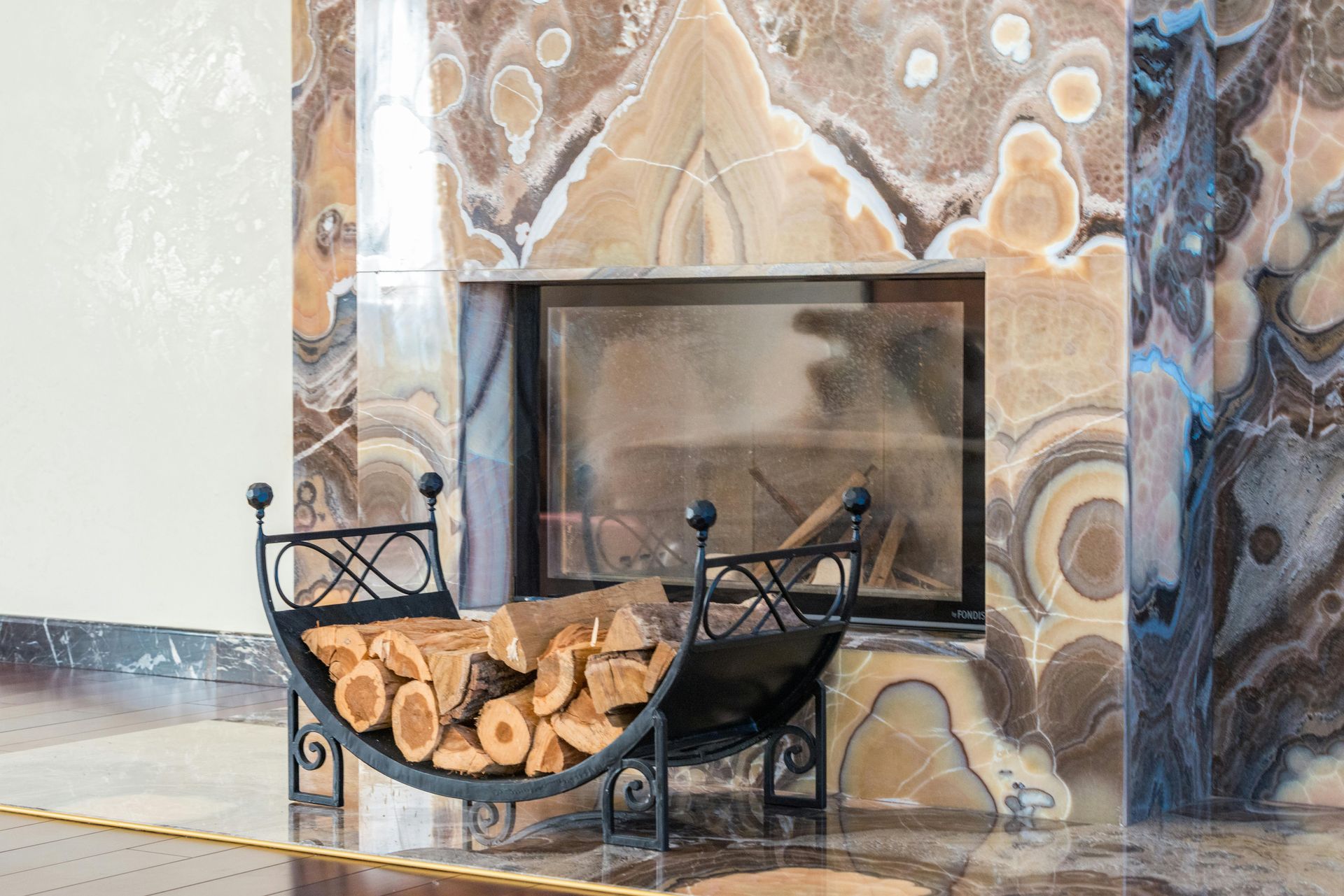 Fireplace with stone surround, firewood in a black metal holder.