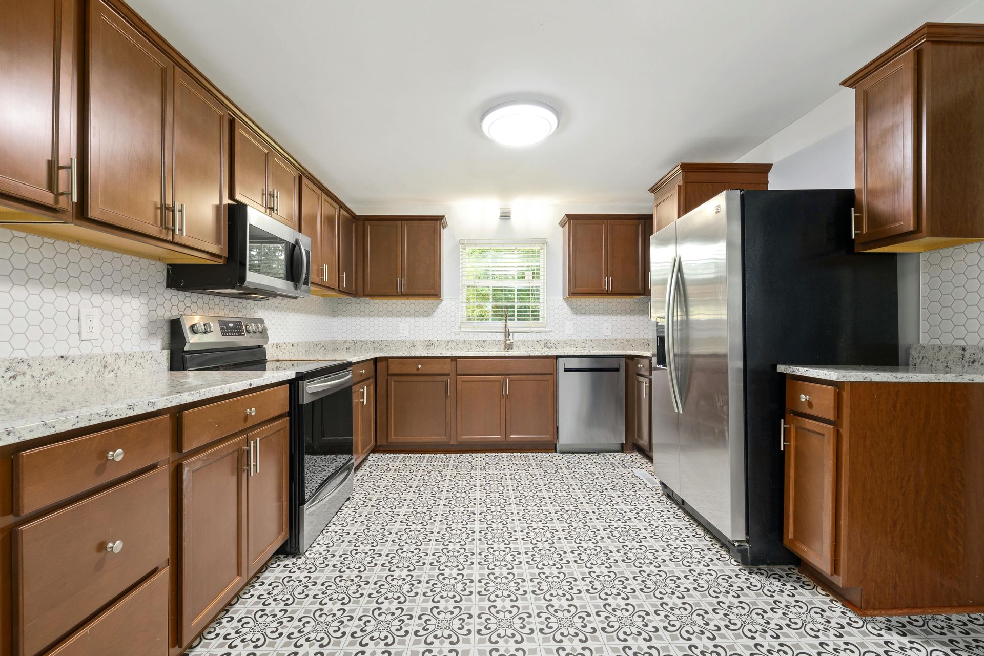 Kitchen with brown cabinets, stainless steel appliances, speckled countertops, and patterned tile floor.