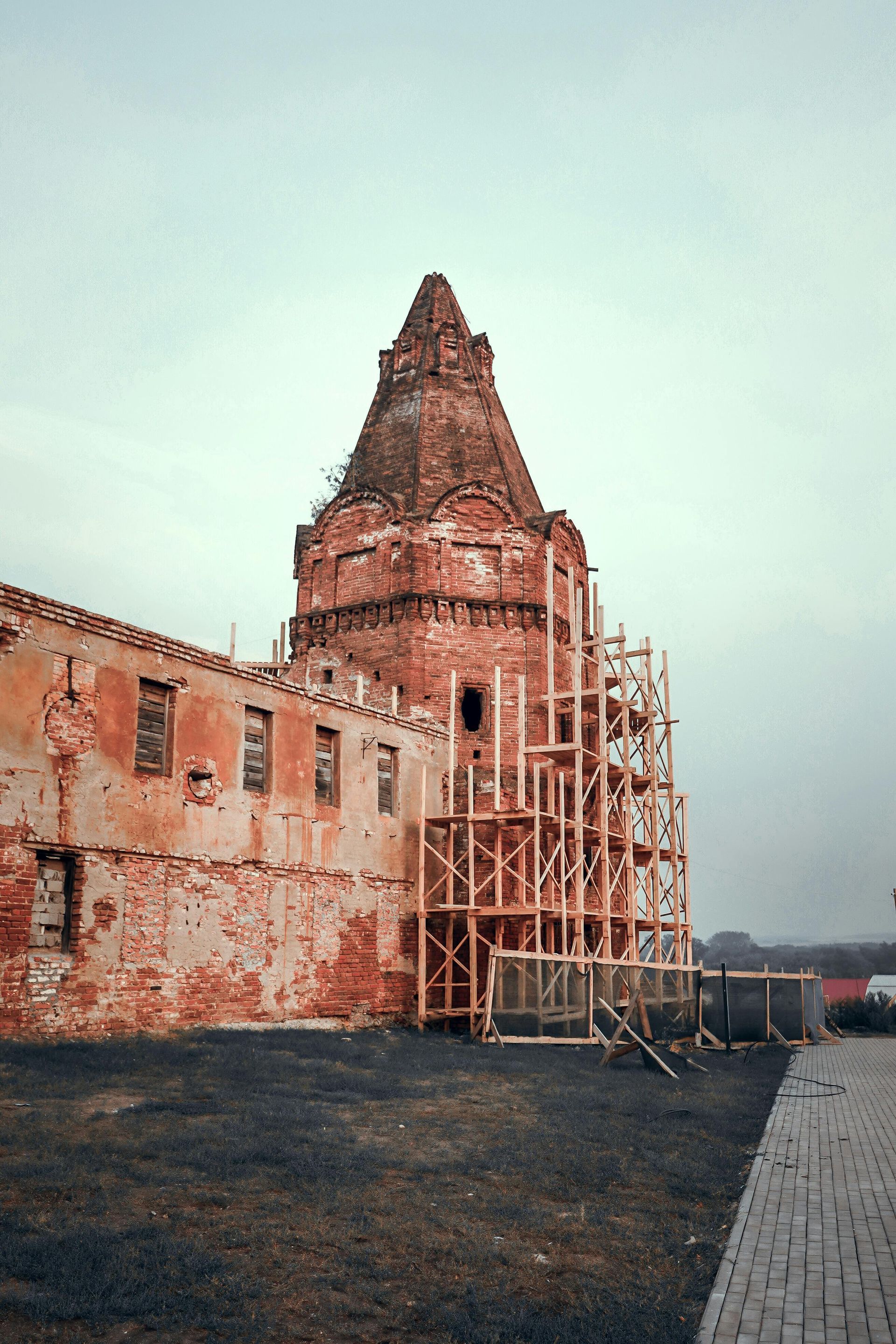 Brick tower and building under renovation on overcast day. Wooden scaffolding surrounds the tower.