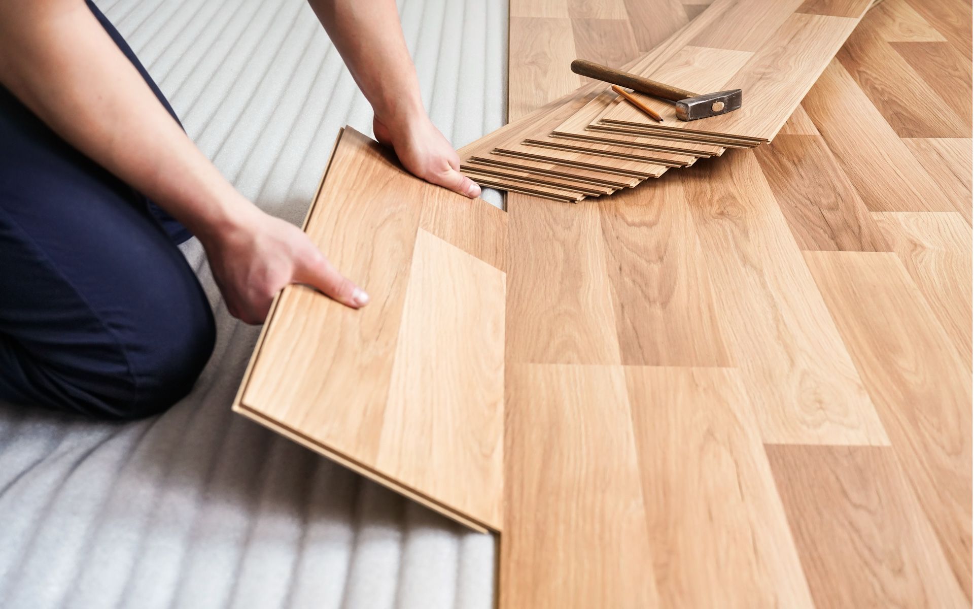 A person is installing a wooden floor with a hammer.