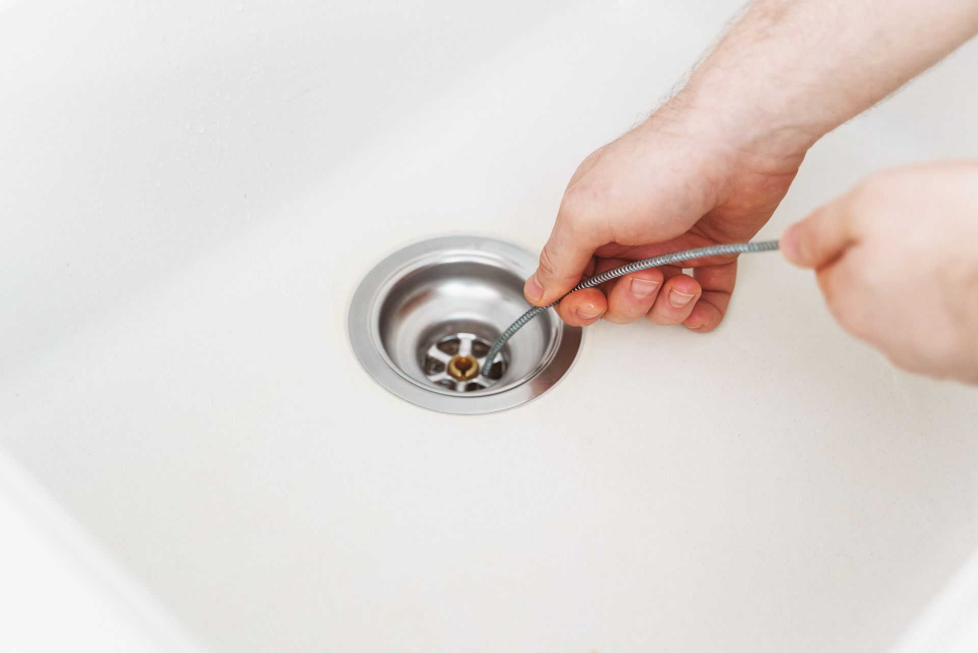 A person is cleaning a sink drain with a spoon.