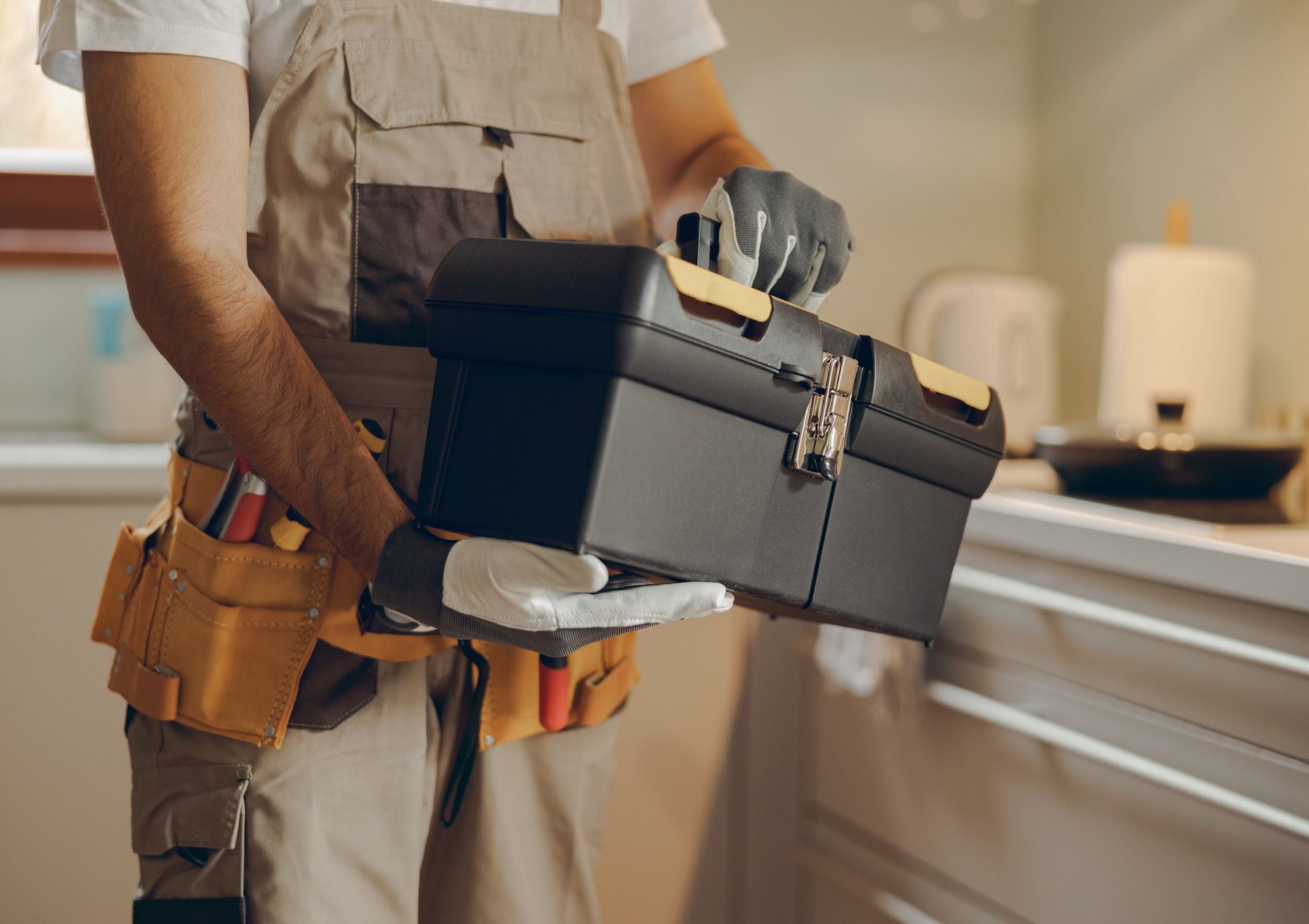 A man is holding a toolbox in a kitchen.