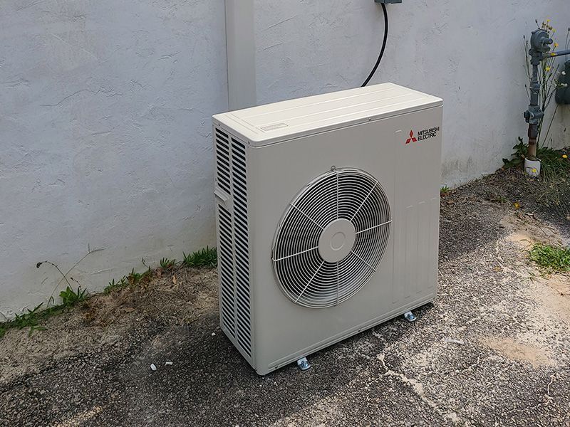 Mitsubishi outdoor AC unit against a white wall.