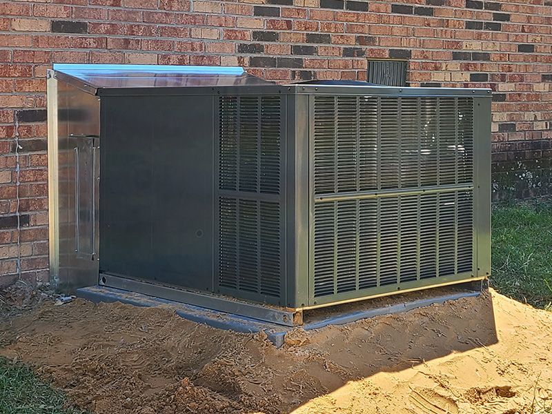 Black outdoor air conditioner unit next to a brick wall.