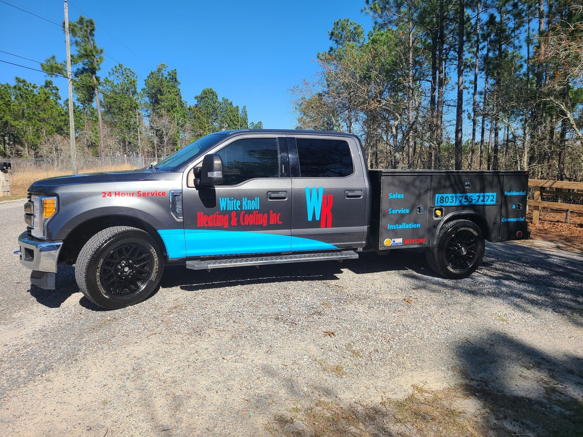Gray work truck with black wheels and blue and red company graphics, parked outside on gravel.