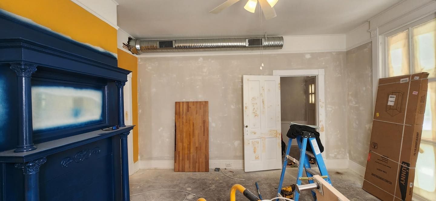 Room renovation in progress, featuring a dark blue fireplace, yellow accent wall, and construction materials.