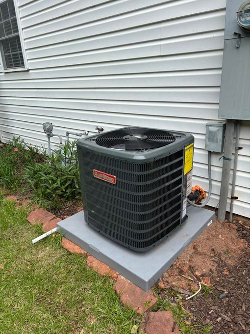Goodman air conditioning unit on a concrete pad next to a house with white siding and electrical box.