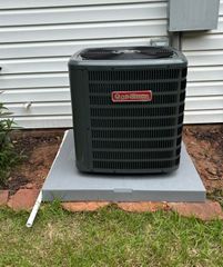 Goodman air conditioning unit on a concrete pad next to a house with a white exterior.