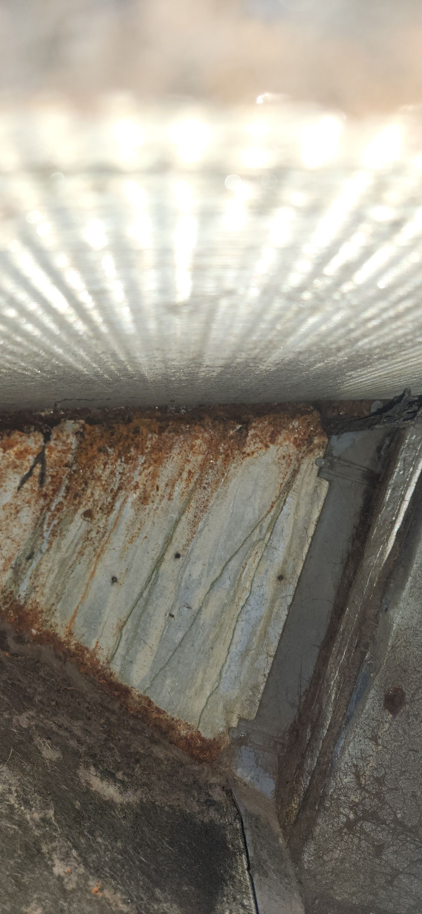 Close-up view of weathered, rusty metal surface with linear textures, possibly a structure's underside.