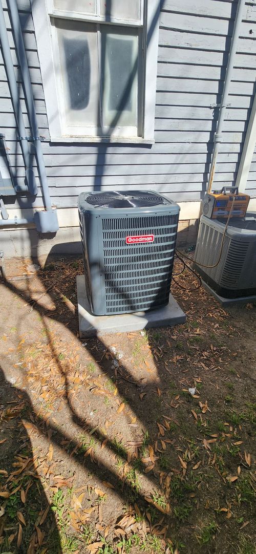 Outdoor air conditioning unit with gray exterior against a gray building with a window.