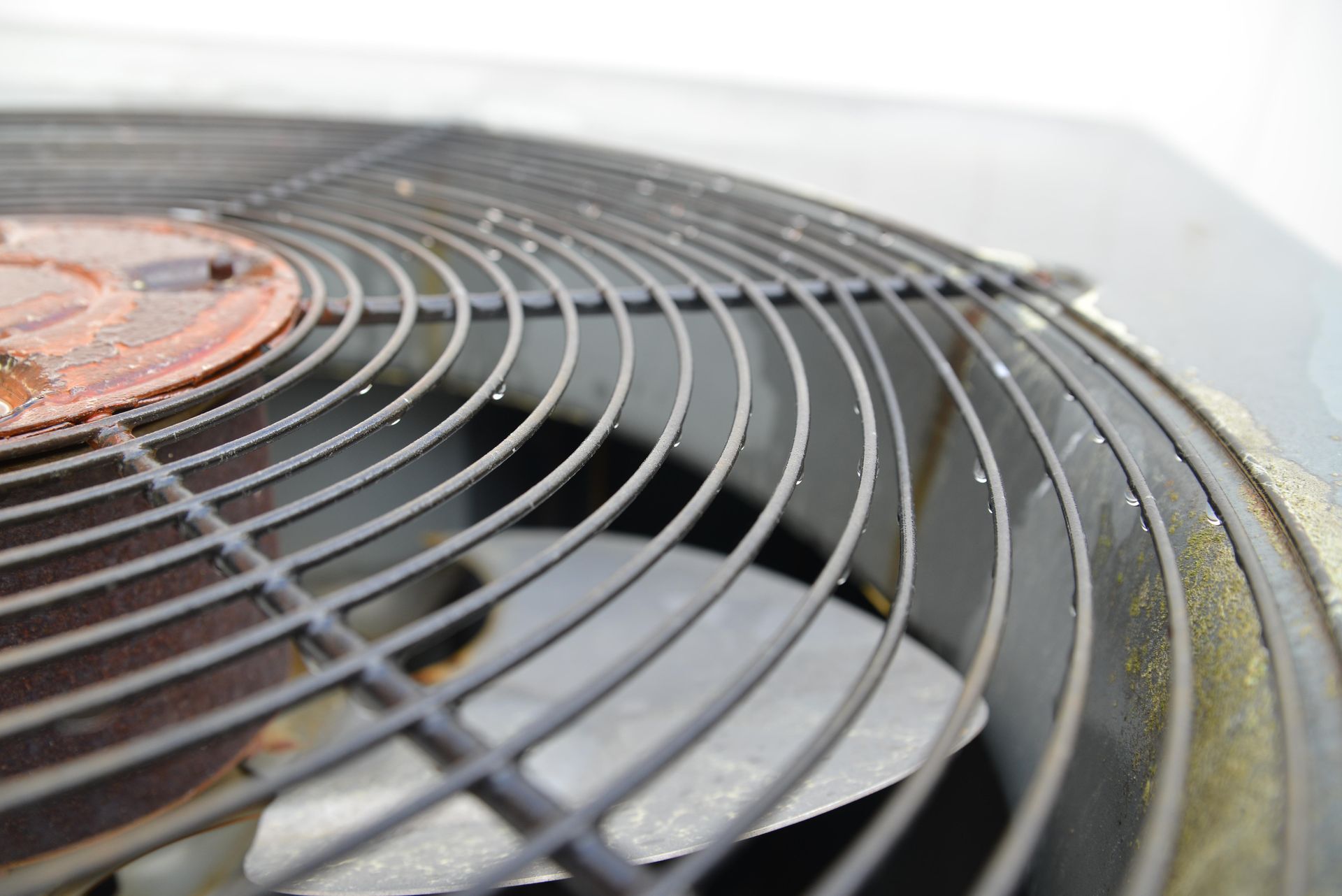 Close-up of a dusty metal fan grille on an outdoor air conditioner unit.